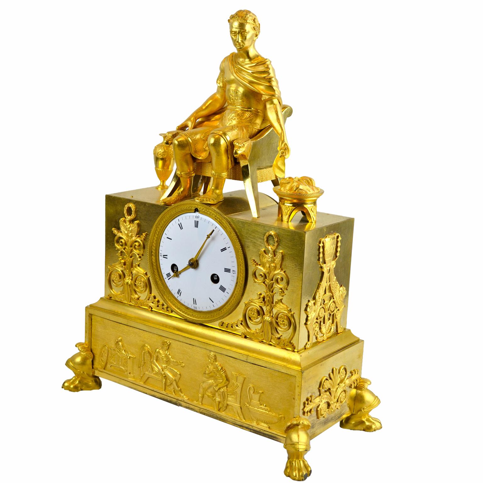 A French Empire gilt bronze clock showing a Caesar (resembling Napoleon), seated on a classical throne. He is slightly leaning to one side as he is in the process of burning a document in a brazier set on the floor on the left side of the throne. A