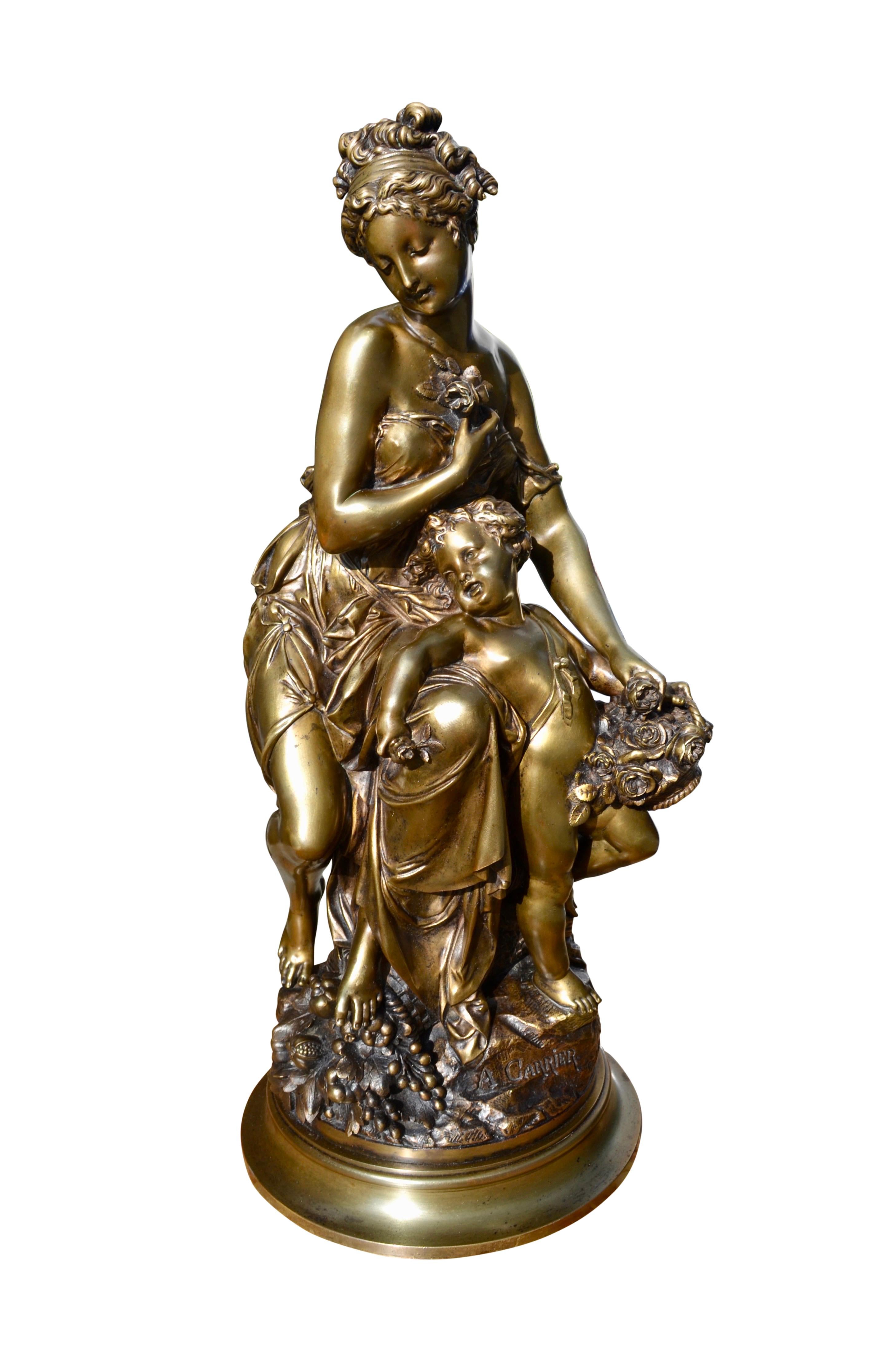 A beautifully cast gilt bronze statue of a classically draped seminude maiden representing Venus sitting on a tree trunk with  her son a nude standing cupid  holding a basket of roses leaning against Venus's left knee. Venus has one hand holding a