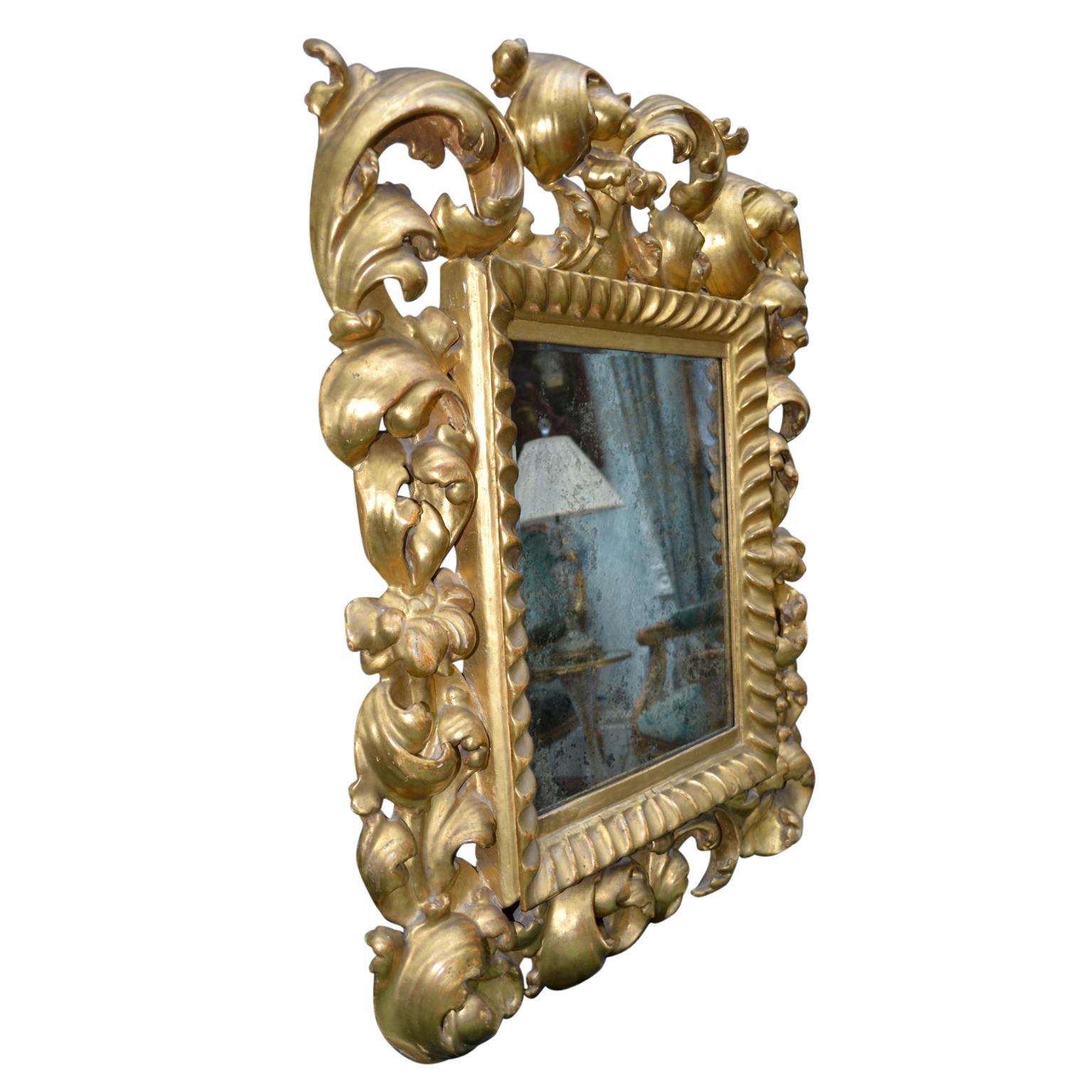 A small scale 19th century Italian Baroque style mirror with a heavily carved gilt wood rococo frame still with its original silvered glass. Losses to the silver backing consistent with age.