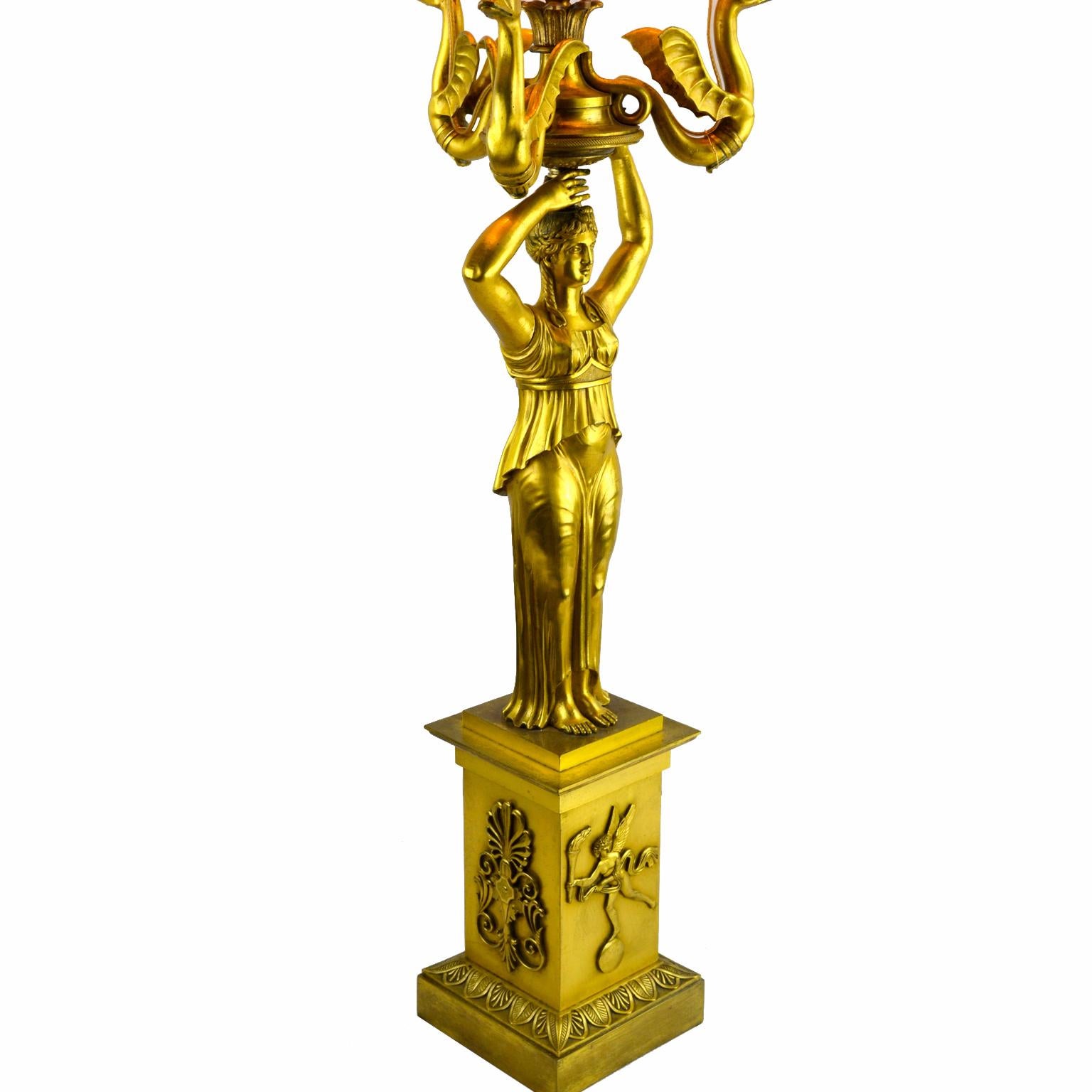 Un candélabre de style Empire russe finement moulé et doré qui a été transformé en lampe ; présentant une jeune fille classique tenant en l'air trois hippocampes ailés terminés par des becs de bougie autour d'un bec de flamme central ; la base