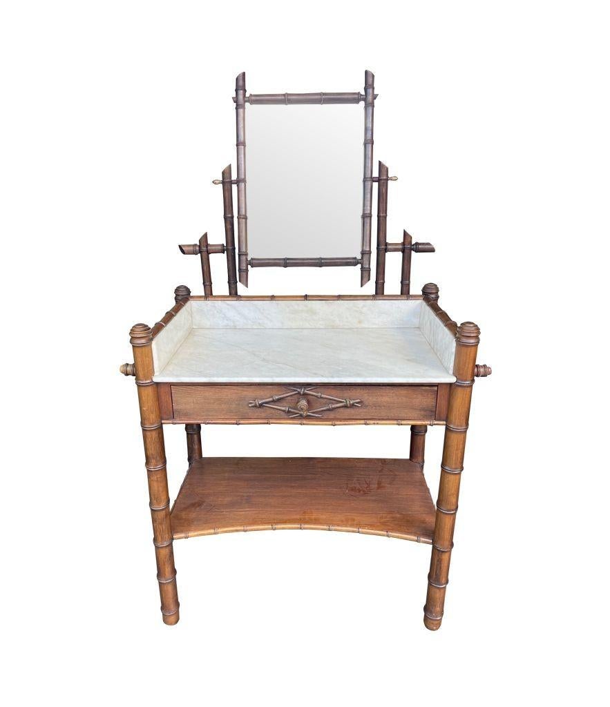 A 1920s faux bamboo and white Carrera marble dressing table with central hinged mirror with brass acorn fixings above a central drawer and shelf, with towel rails on each side.