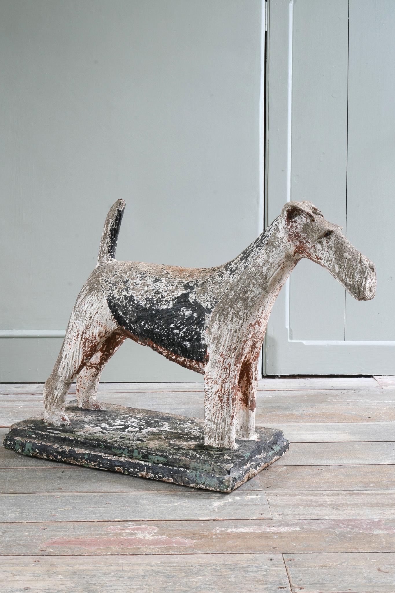 A composition stone Fox Terrier standing with an upright tail.

Remnants of its first painted surface decoration and both glass eyes.