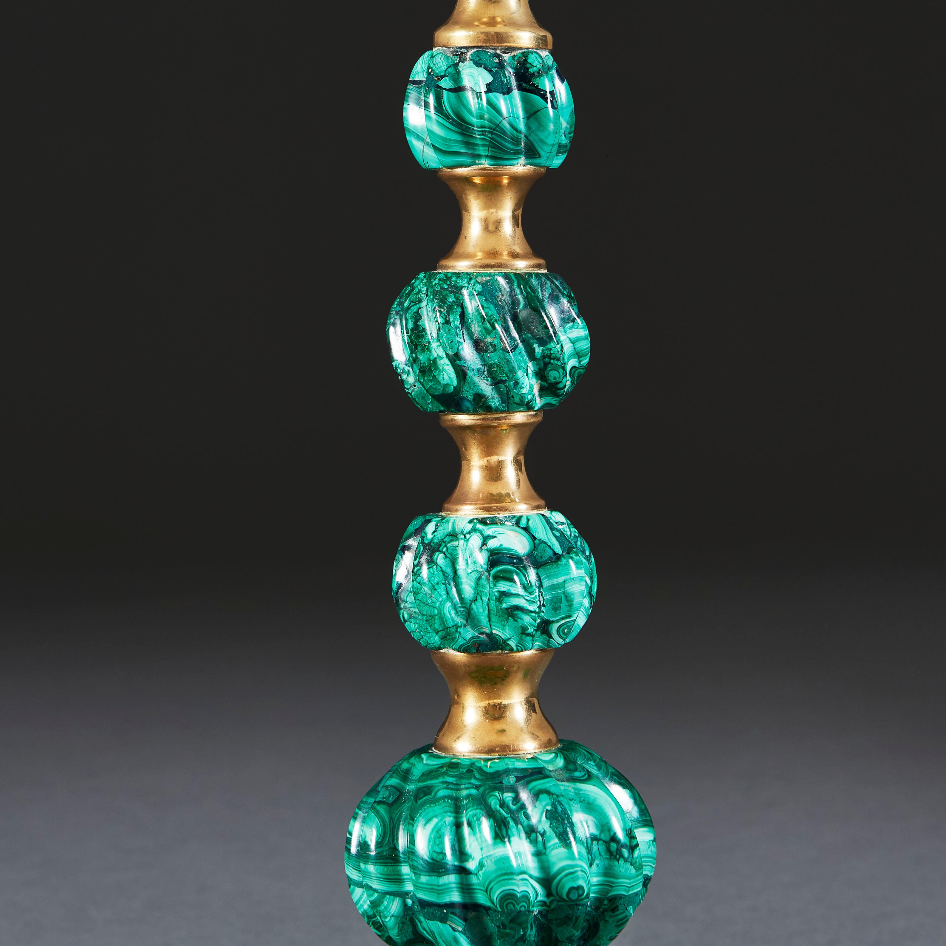 An unusual early 20th century lamp formed of stacked gadrooned green malachite beads of increasing scale, spaced with brass concave metalwork elements.

Currently wired for the UK. 

Lampshade not included.