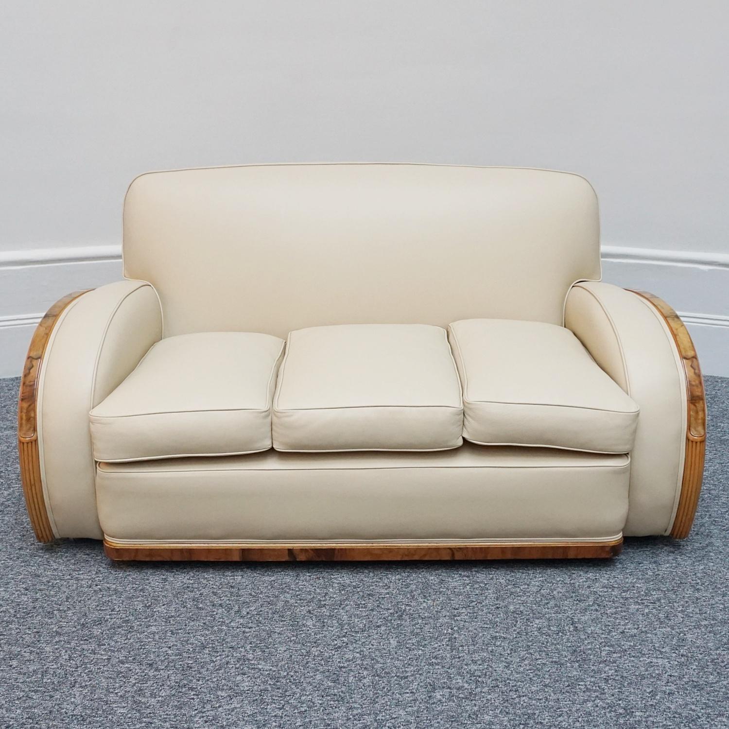 An Art Deco Tank Sofa by Heal's of London. Burr and solid walnut banding with reeded lower section. Re-upholstered in cream leather and contrasting faux suede. 

Dimensions: Sofa H 80cm W 163cm D 74cm Seat H 49cm

Origin: English

Date: Circa 1935