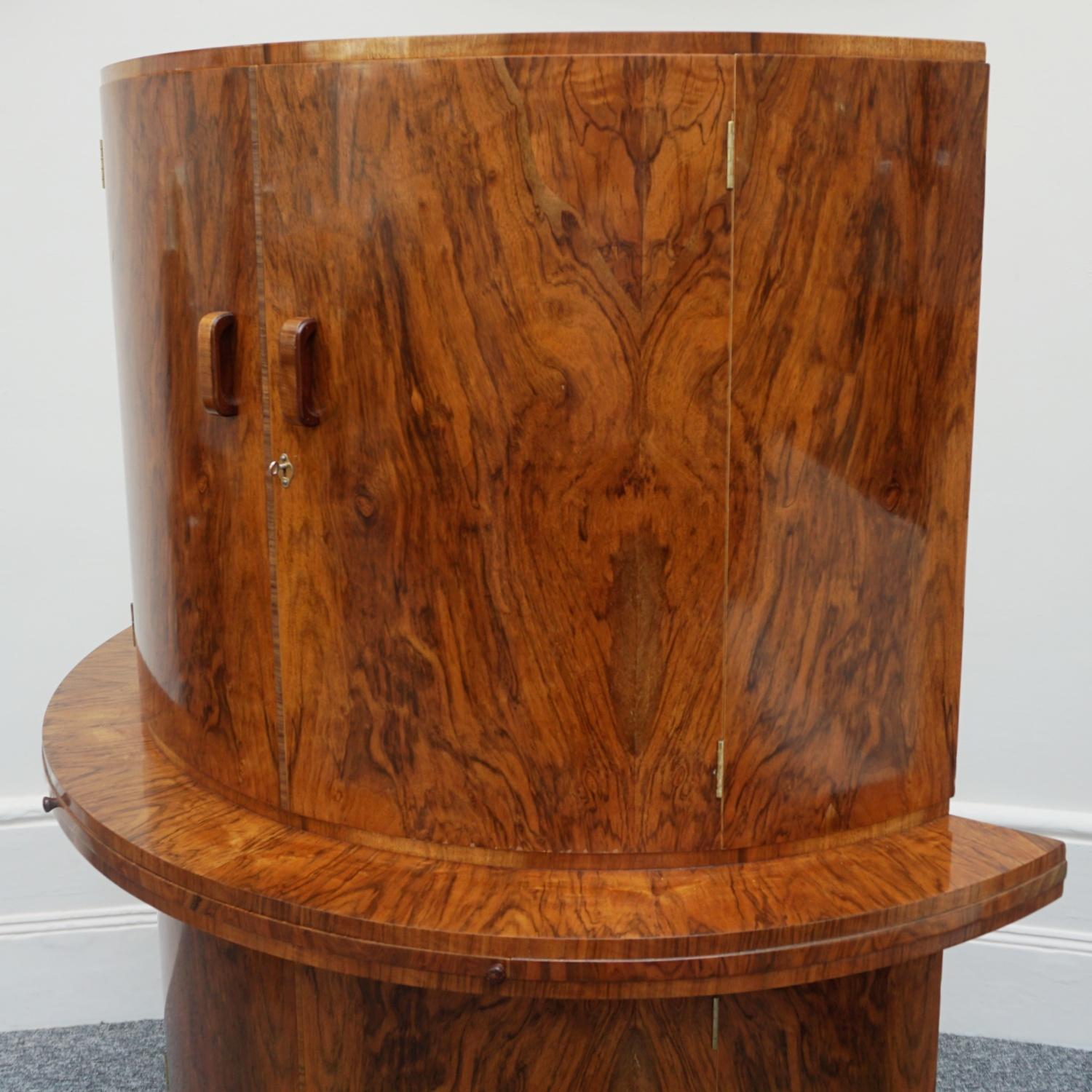 An Art Deco cocktail cabinet by Gold Feather Products retailed by Wolfe & Hollander Ltd London. Burr walnut veneered with figured walnut banding and top. Mirrored shelved interior to top, with a shelved, lower cabinet with bottle