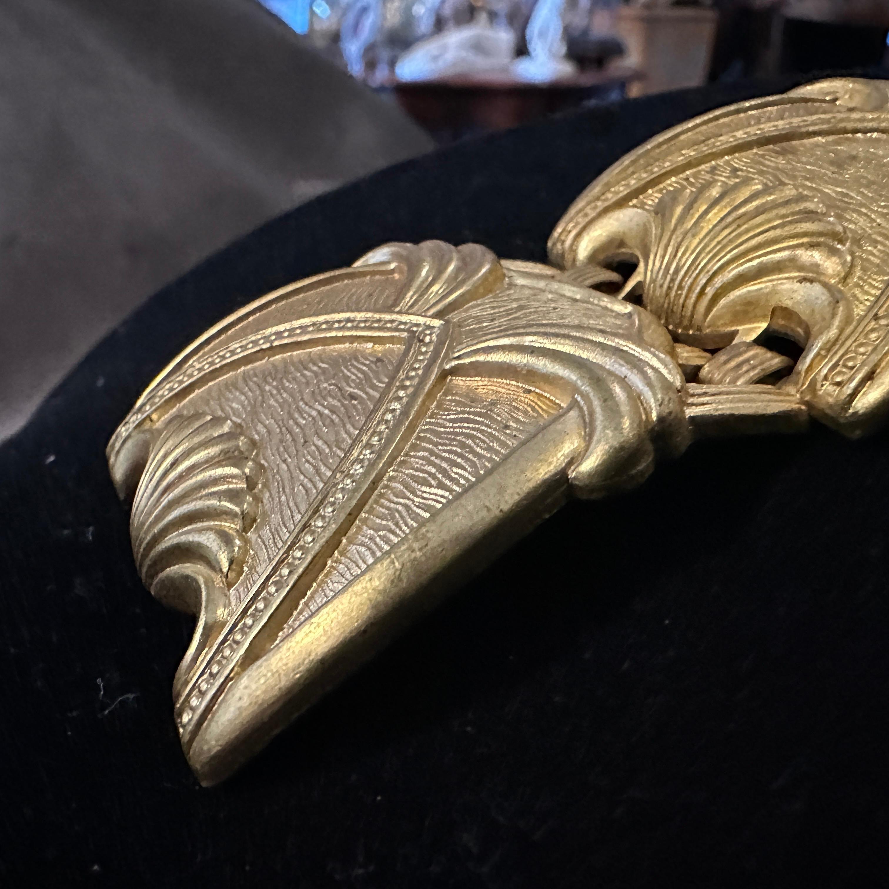 Esta pulsera de metal dorado Art Decó de los años 30 presenta un llamativo diseño geométrico, característico de la estética audaz y simétrica de la época. La pulsera está formada por paneles enlazados, cada uno de ellos con forma de concha
