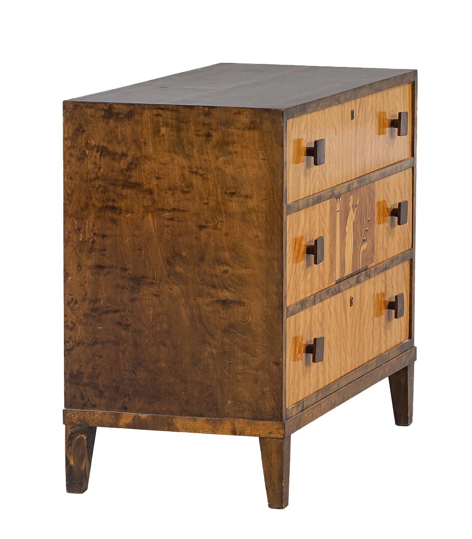 A 1930s Swedish marquetry chest with highly figured birch. The three drawers with walnut-colored square pulls, and the center drawer featuring a classical female figure. The whole piece supported by square and tapered legs. Circa 1930s.