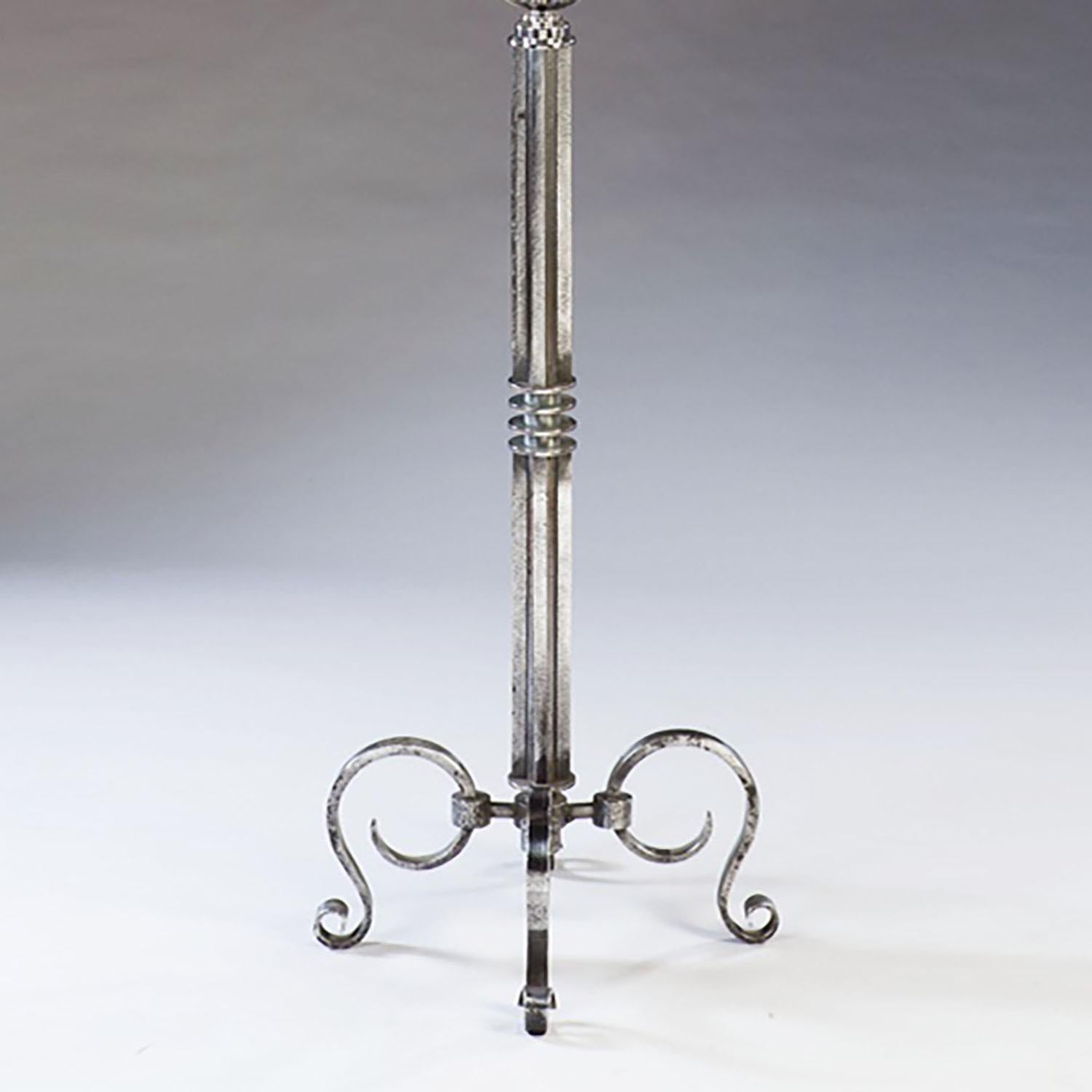 A rare and unusual modernist iron lampstand, fashioned as a column with multiple ribs and collars and a central Astrolabe, standing on a tripod of scroll legs and surmounted by a stylized globe with a ribbed cup above. Attributed to Gilbert