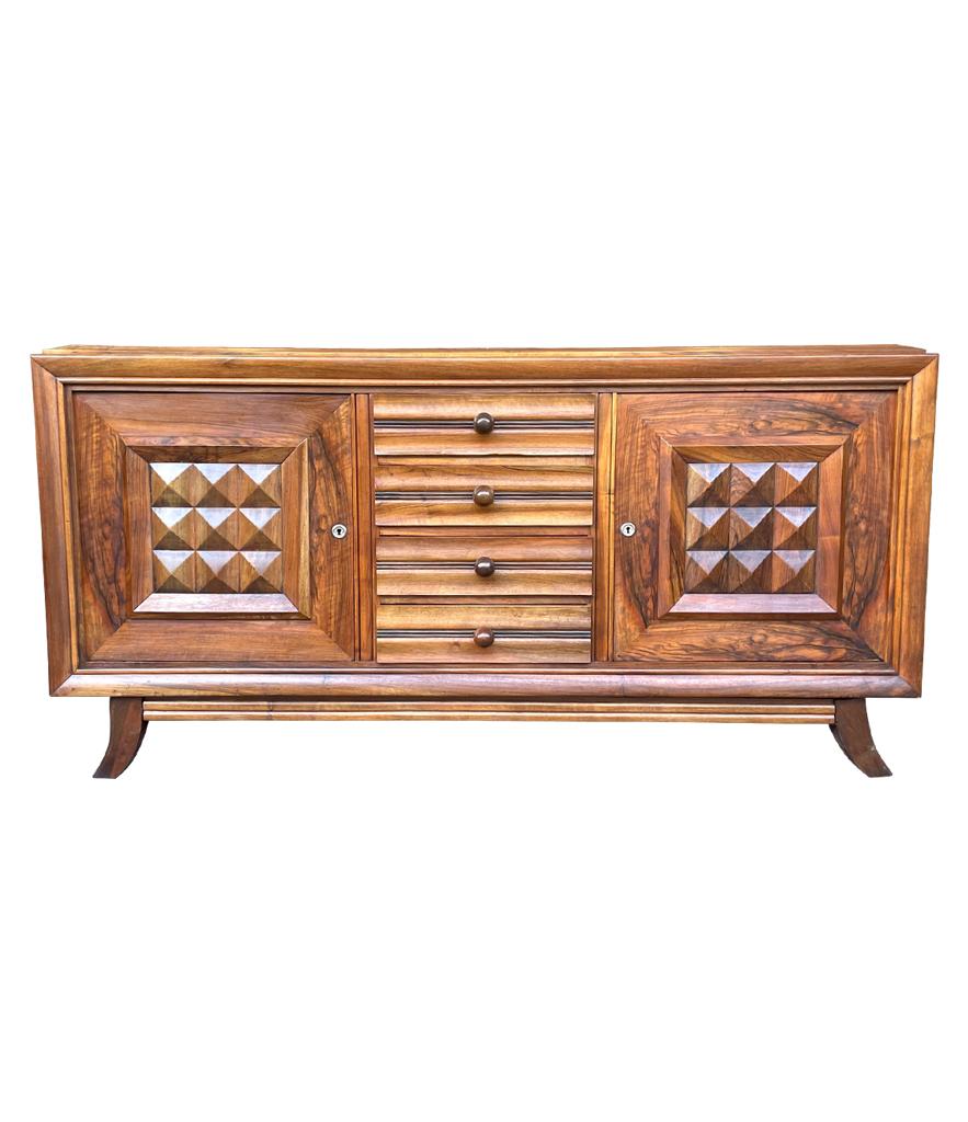 A fabulous 1940s walnut and oak sideboard by Charles Dudouyt with two doors each with central geometric relief design, both doors with orignal key and locks. 
These sit either side of four central drawers with characteristic Dudouyt large, slightly