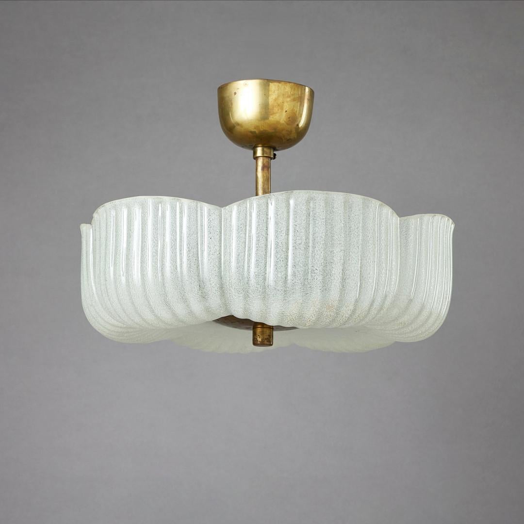 A brass and glass pendent attributed to Arvid Böhlmarks Lampfabrik, Sweden, circa 1950s. The fixture features a beautifully patinated brass frame with a hemispherical ceiling cup and central support rod, anchoring a substantial, scalloped glass
