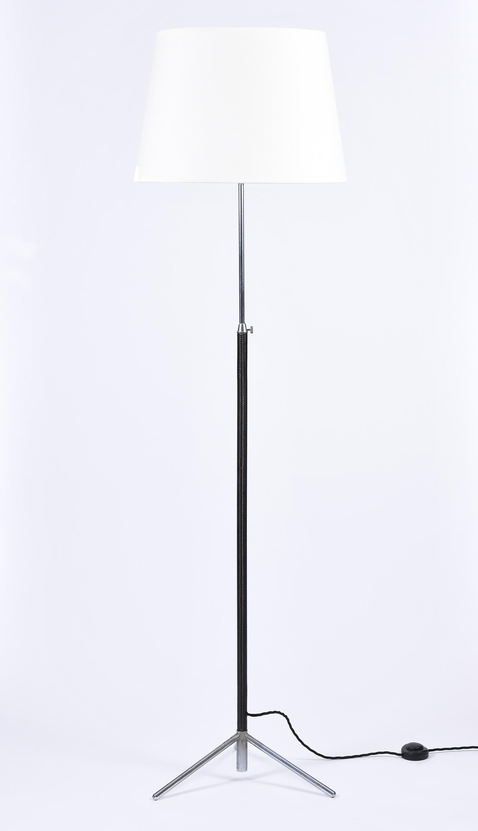 A saddle stitched black leather and nickel-plated brass tripod floor lamp, in the manner of Jacques Adnet
with a telescopic stem and a bespoke ivory fabric tapered shade
France, circa 1950.