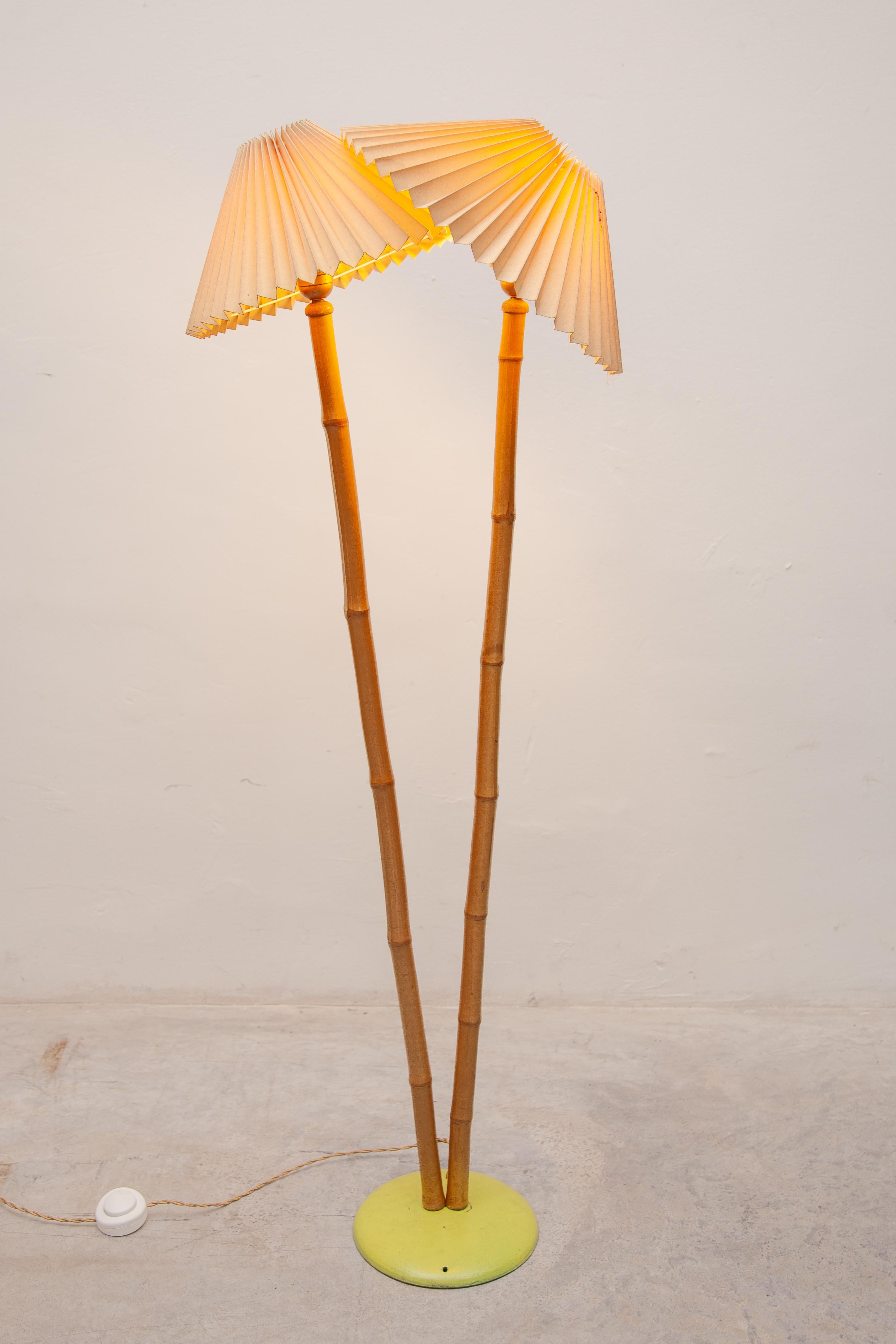 Una original lámpara de pie de los años 50, diseñada y fabricada en el sur de Francia. Esta antigua lámpara de pie presenta un elemento retorcido con dos tallos de bambú unidos a una base redonda de metal pintado de amarillo con dos pantallas. La