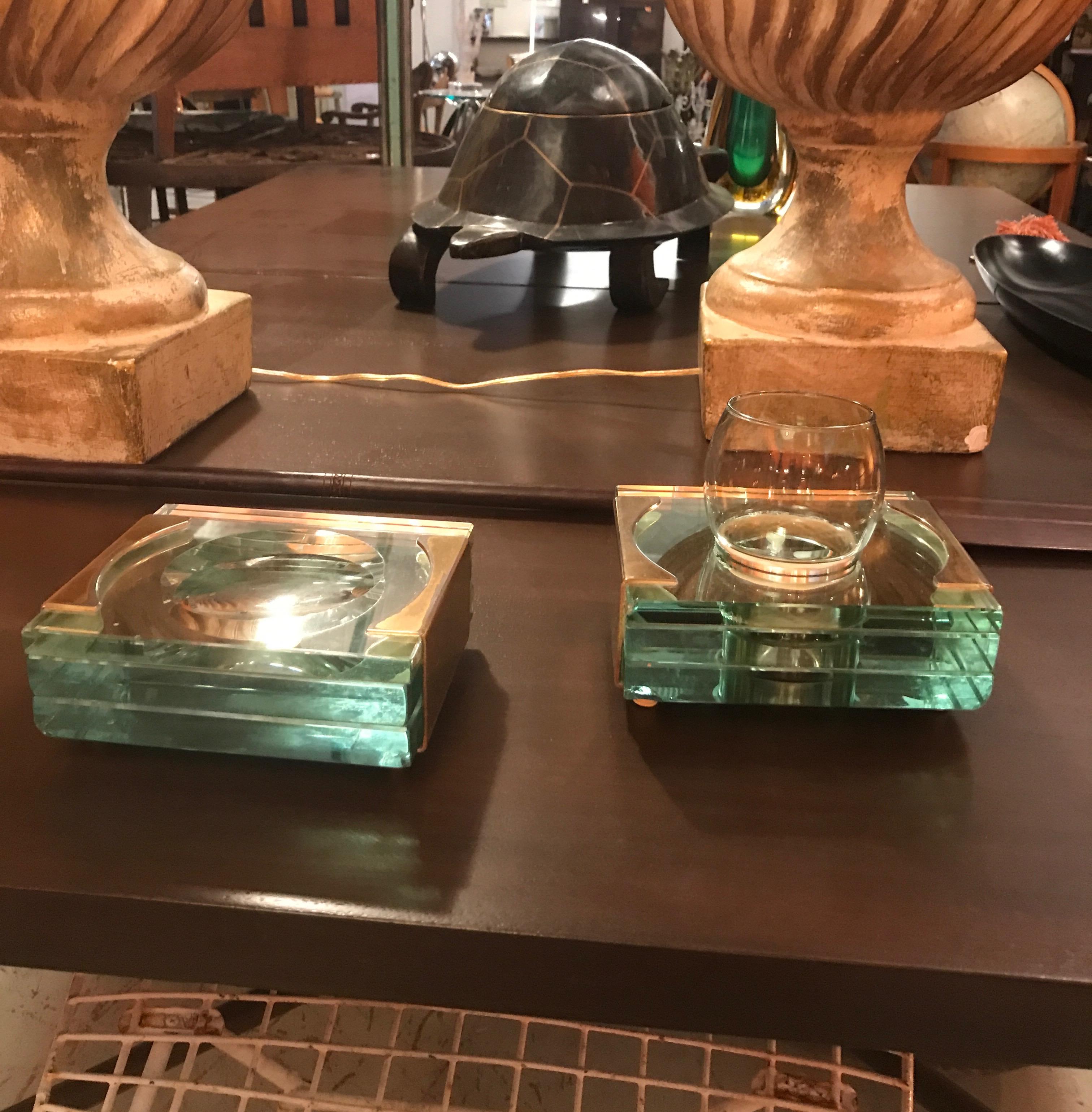 A three piece 1950’s Italian green glass and brass toned bathroom set composed of a cop holder with original smoked charcoal colored glass cup with original protective cloth band, and a convex mirrored stand for tools brushes tweezers etc attributed