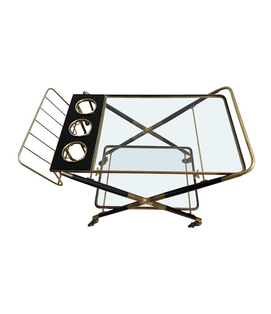 A 1950s rare bar trolley of black lacquered wood and brass by Cesare Lacca with rare top bottle holder and magazine rack on orignal brass castors with two glass shelves, the lower being a removable tray.