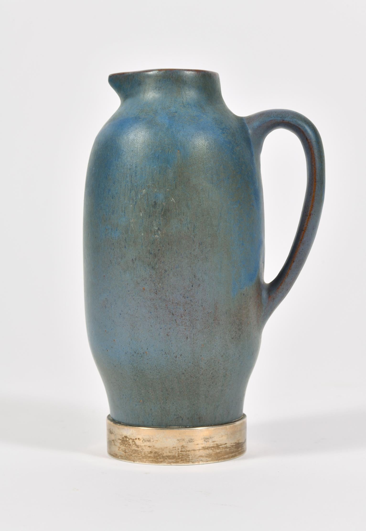 A mottled blue stoneware jug, on a solid silver base.
Bearing two Spanish silver hallmarks: the five-point star silver fineness mark for 915/1000 purity (plata de ley) and the city of Barcelona assay office mark. Also bearing the ceramicist