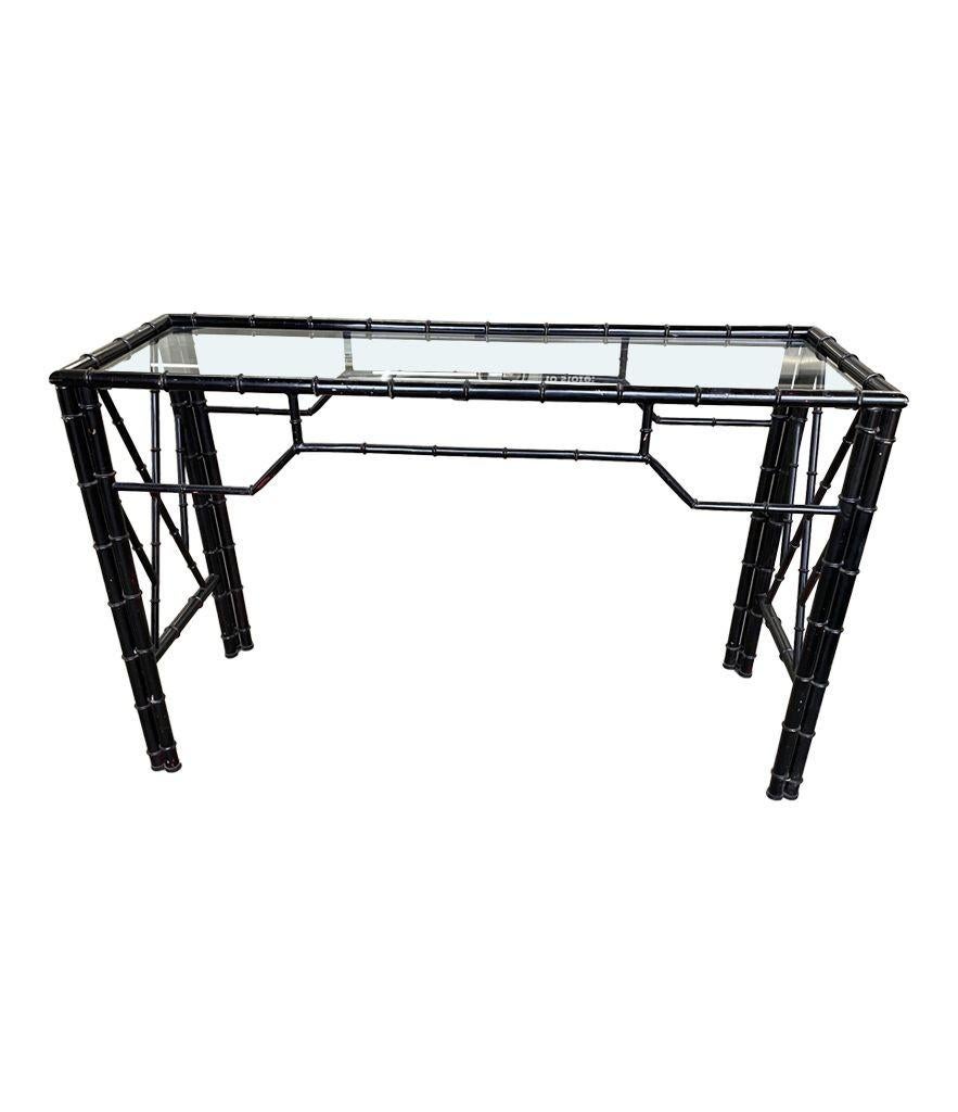 A 1960s faux bamboo black lacquered metal console table with glass shelf.