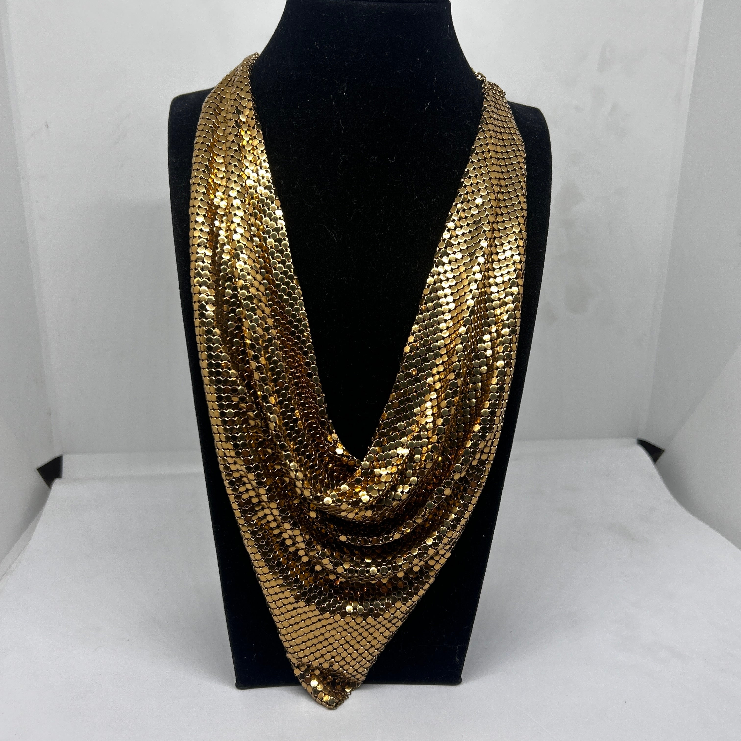 Questo versatile accessorio vintage è realizzato in una maglia dorata scintillante, composta da piccoli dischi metallici collegati tra loro che creano un design fluido e drappeggiato. La collana pende liberamente intorno al collo, formando morbide