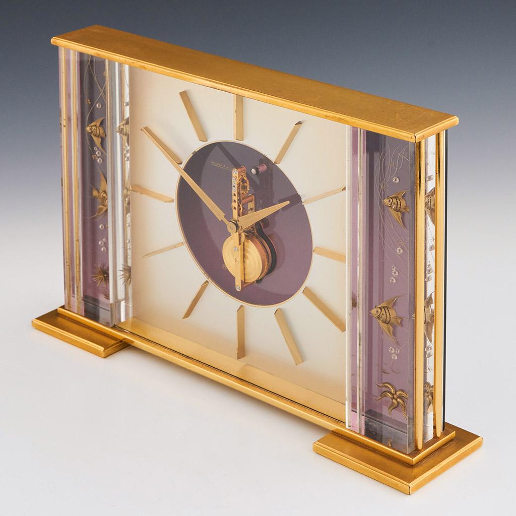A mid-century Jaeger-LeCoultre marina Fish mantel clock. Central square dial with an open centre revealing skeletonised 8 day movement, flanked by inset brass angel fish and marine life . Set within.a brass and perspex case. Together with receipt