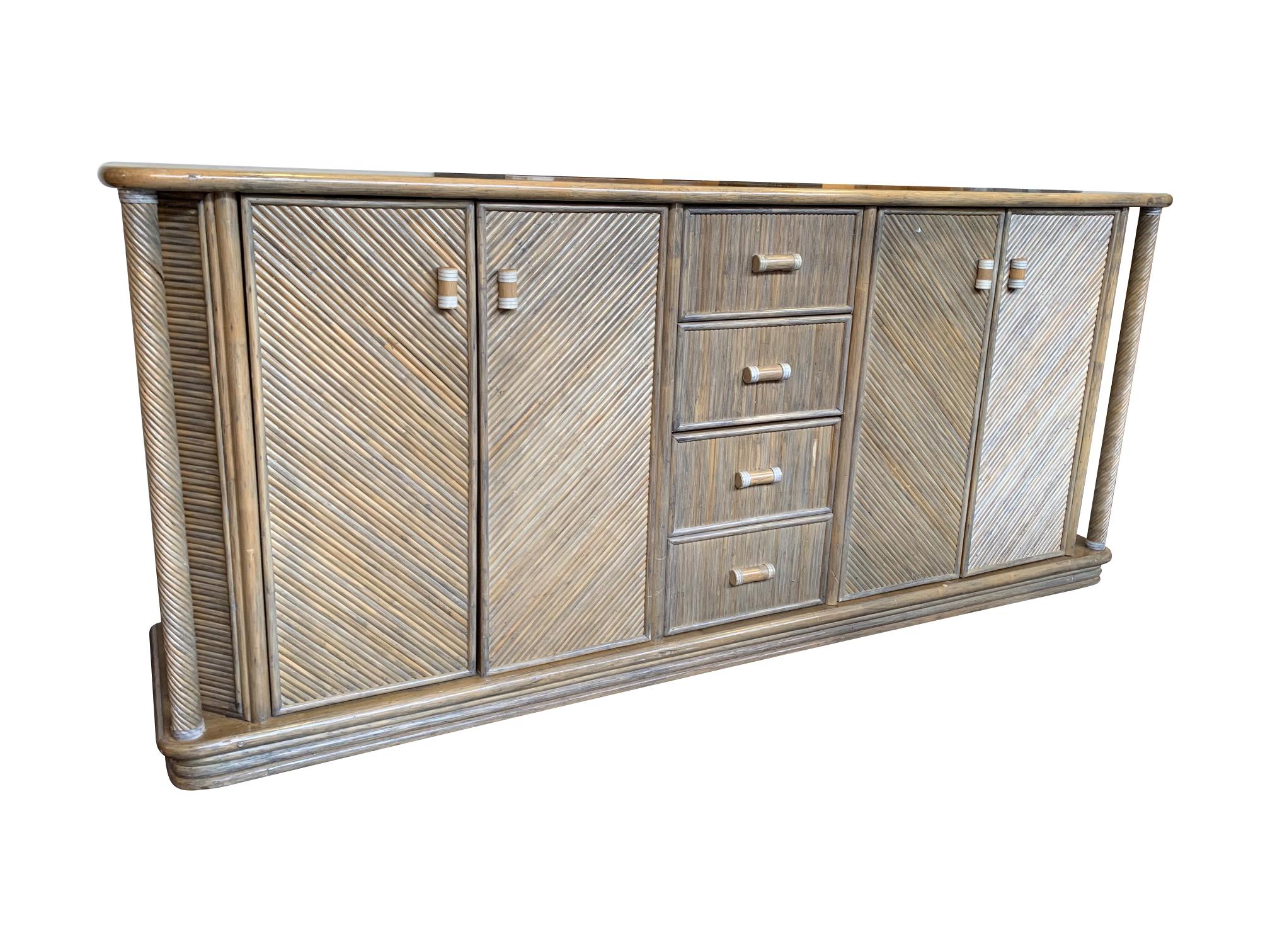 A 1970s French Riviera bamboo credenza with four cabinet doors and four central drawers with bamboo and leather handles. There is an interesting corner details on each side with spiraled spindle of bamboo and solid bamboo top.