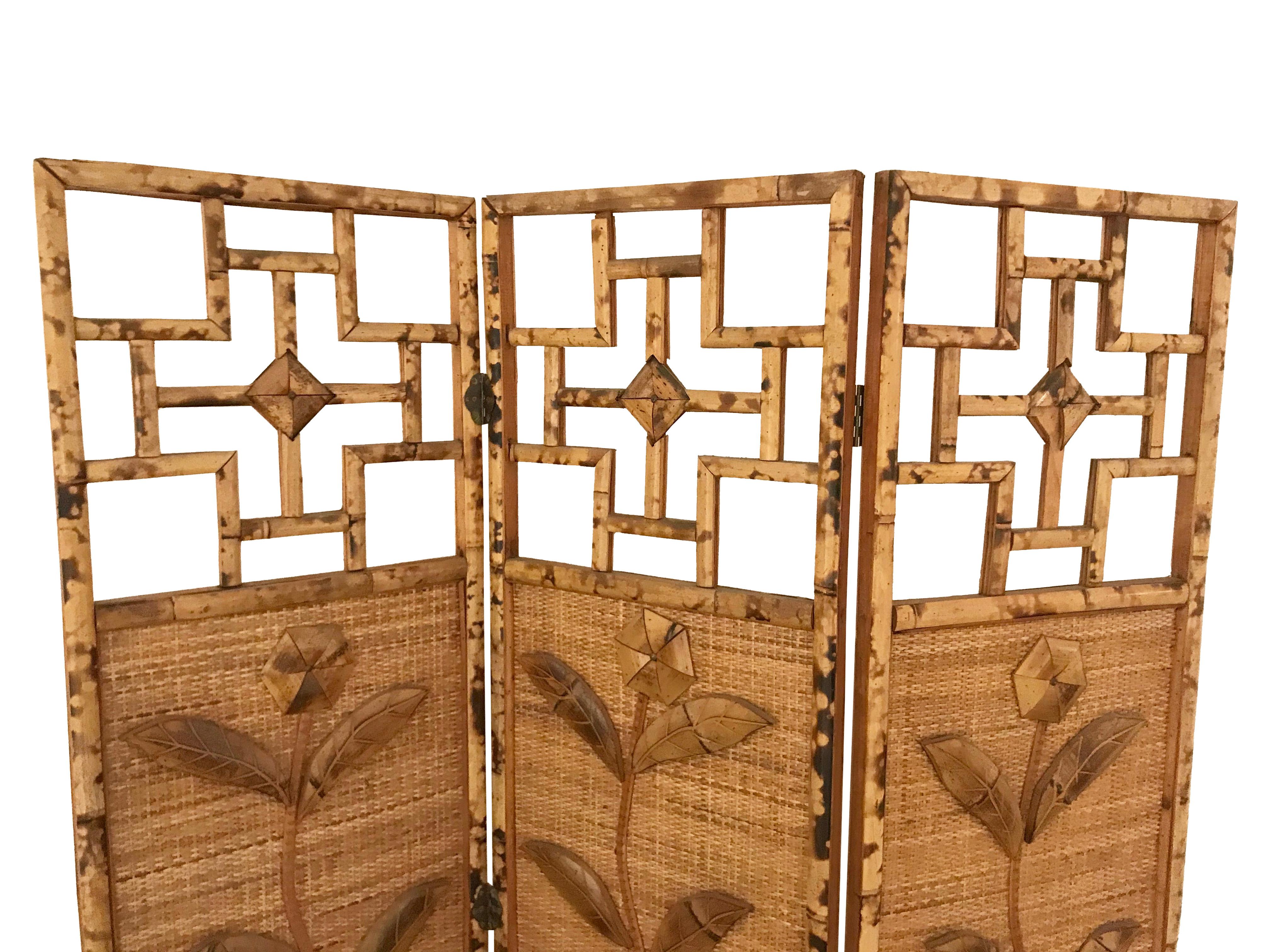 A three panelled French Riviera 1970s rattan and bamboo screen /room divider, with relief flower motifs on the front and back of the central panels, with brass hinges.