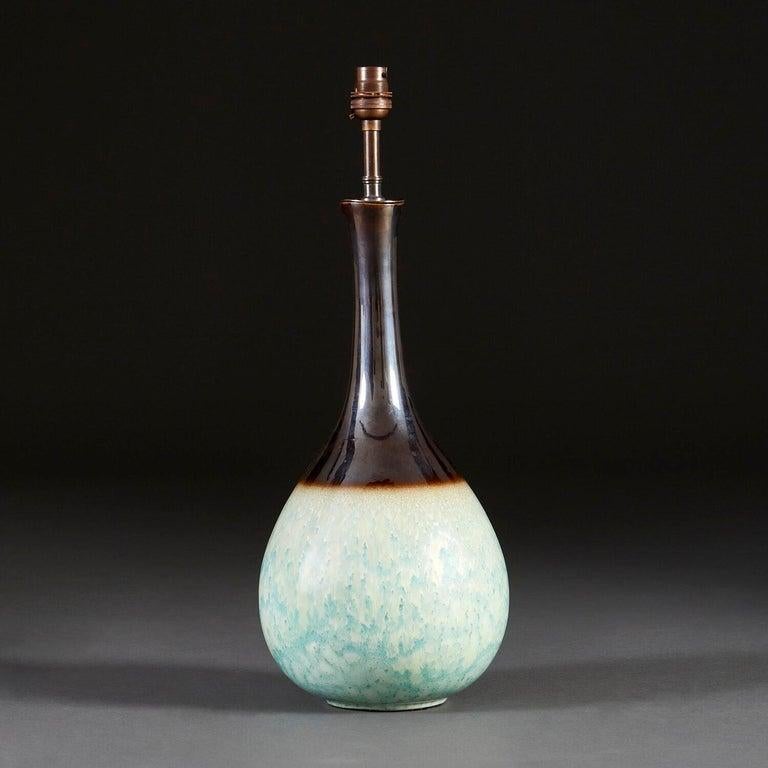 A 1970s studio pottery vase of bottle neck form, with duck egg blue glaze to the body and dark umber glaze to the neck, now converted as a lamp.

Please note that the lampshade is not included, and that the lamp is currently wired for the UK.