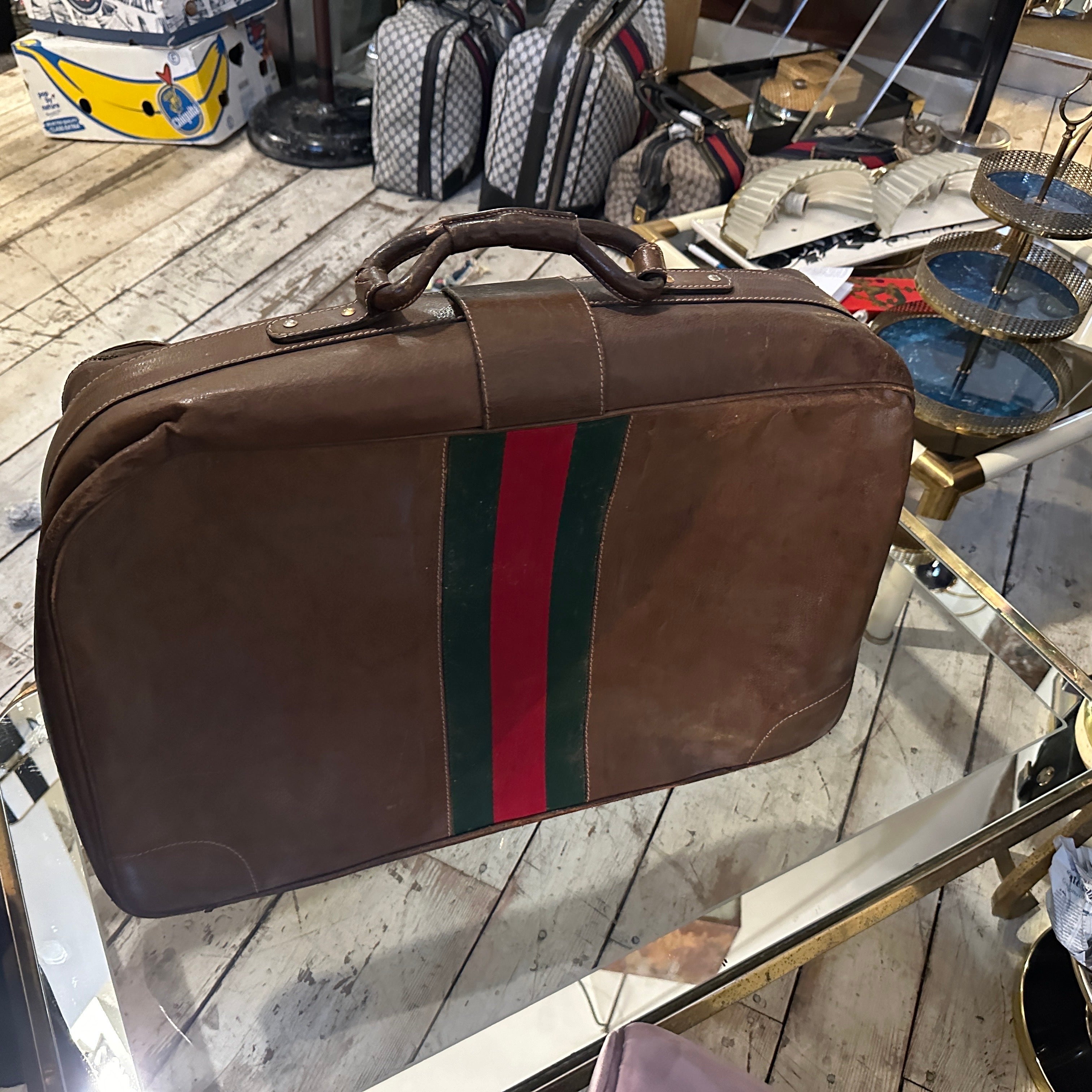 This vintage Gucci suitcase showcases a classic and sophisticated design. Made of high-quality brown leather, it exudes a timeless elegance, enriched with natural patina and subtle wear that gives it character. The signature Gucci green and red