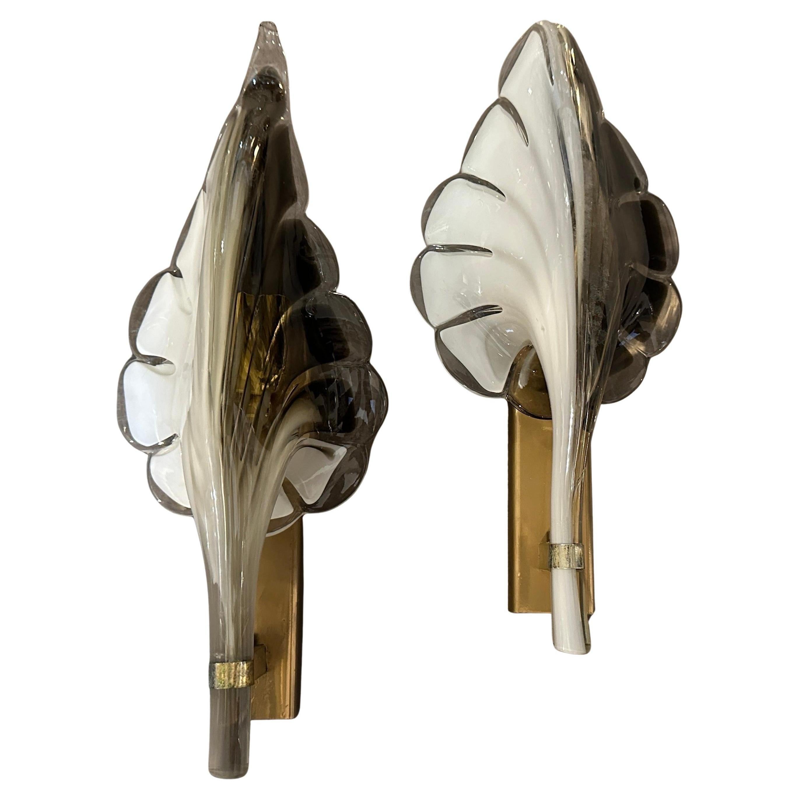 These are 1970s Mid-Century Modern wall sconces designed by Franco Luce. The sconces feature a striking leaf-shaped design made of hand-blown black and white Murano glass, with a translucent finish and soft curves that create a warm inviting glow.