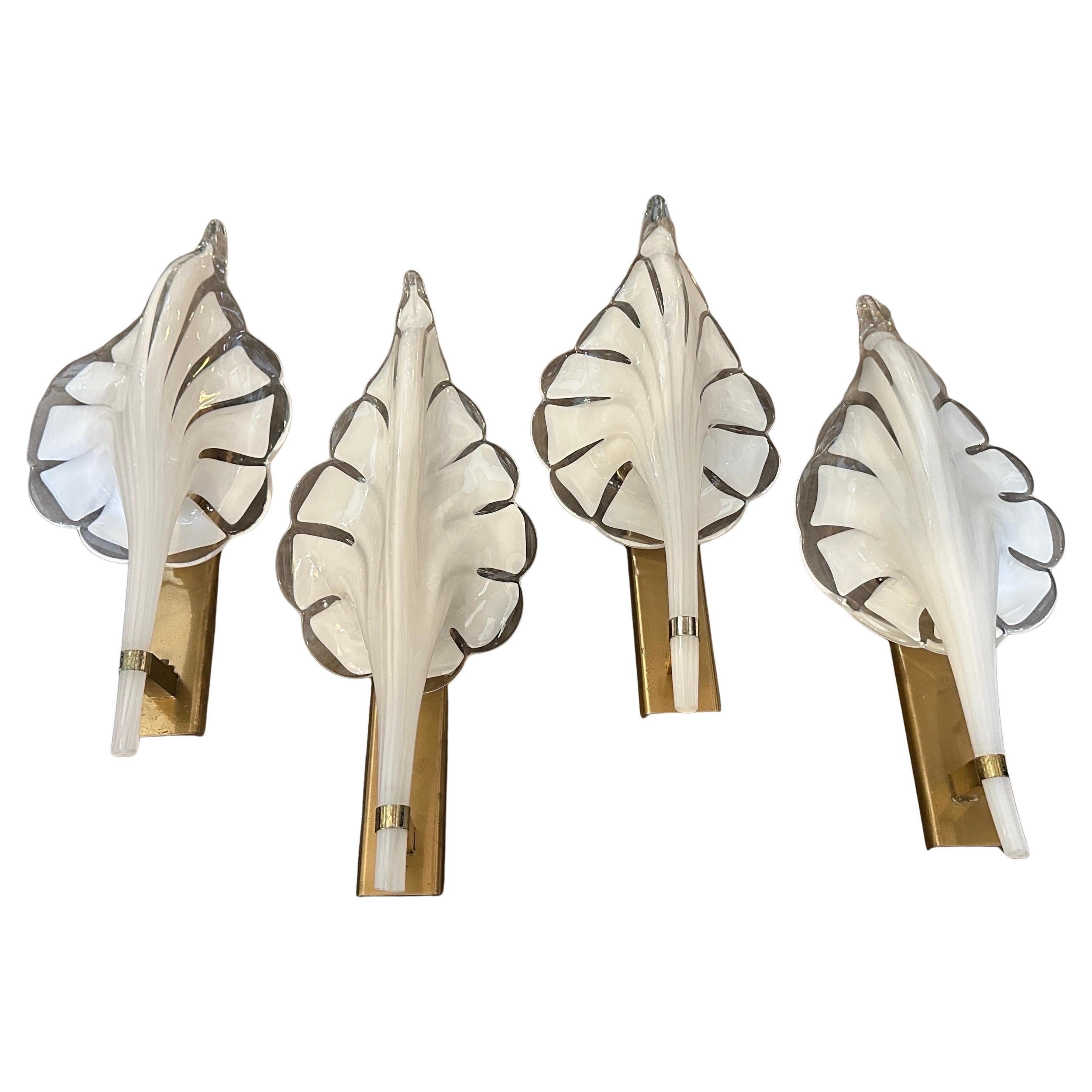 These are 1970s Mid-Century Modern wall sconces designed by Franco Luce. The sconces feature a striking leaf-shaped design made of hand-blown clear and white Murano glass, with a translucent finish and soft curves that create a warm inviting glow.