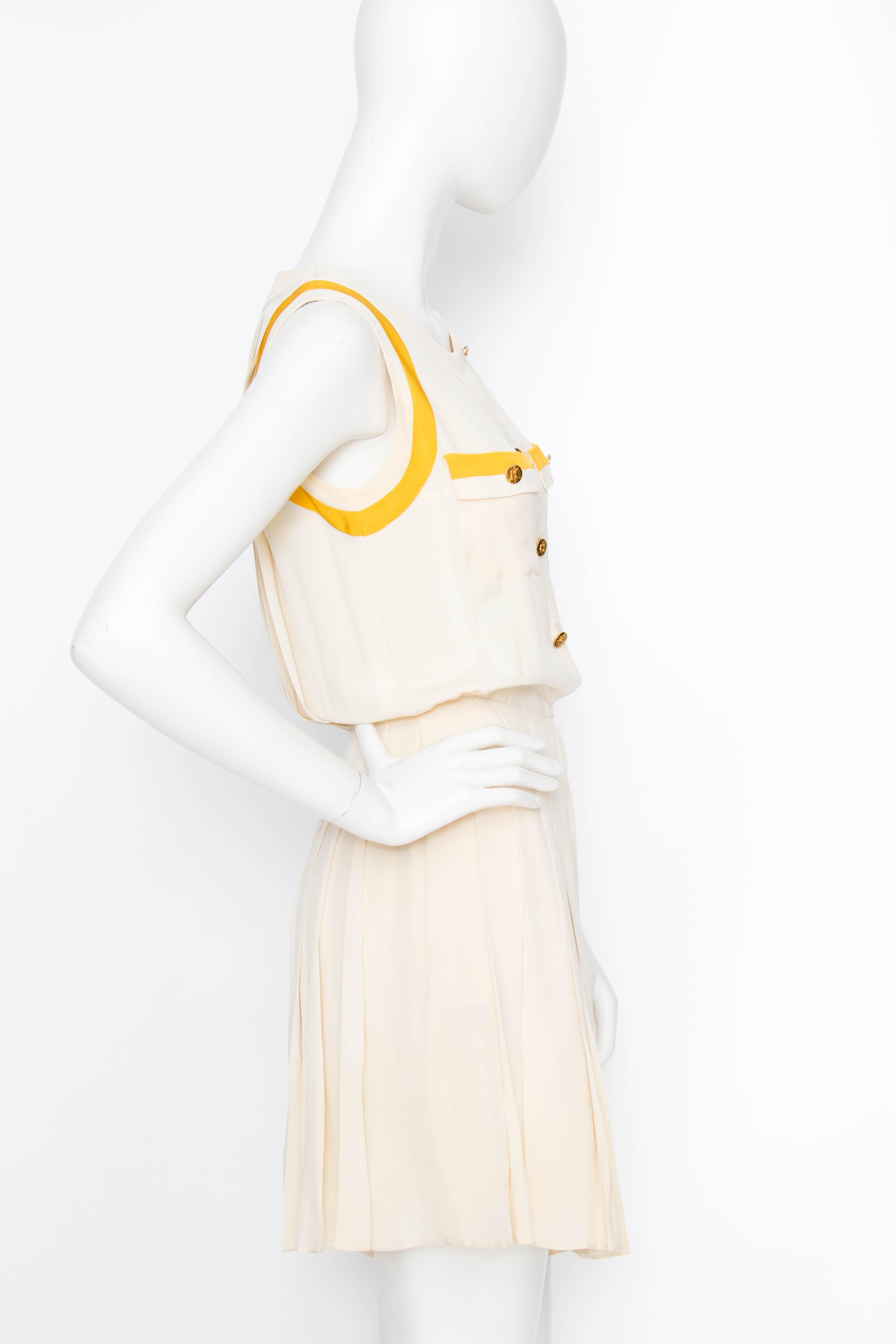A 1980s Chanel creme silk playsuit with yellow piping and gorgeous pleat detail on the back and shorts. Gold-toned Chanel engraved buttons adorn the button down front and the breast pockets. The suit comes with a matching yellow bolero that can be