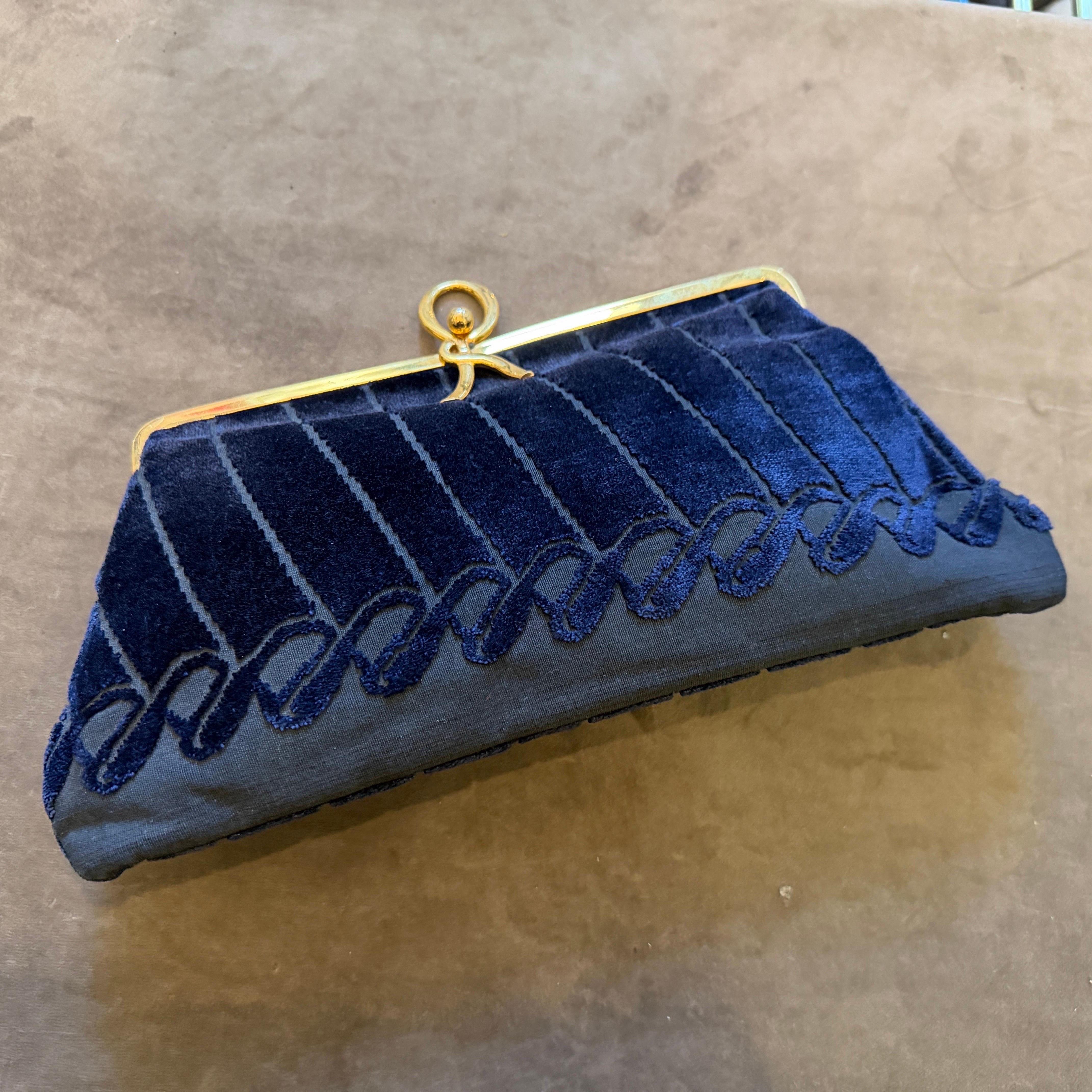 Si tratta di una sofisticata ed elegante pochette da sera vintage degli anni '80 della stimata casa di lusso italiana Roberta Di Camerino. L'esterno è caratterizzato da un ricco corpo in velluto blu notte ornato da un distinto motivo decorativo di