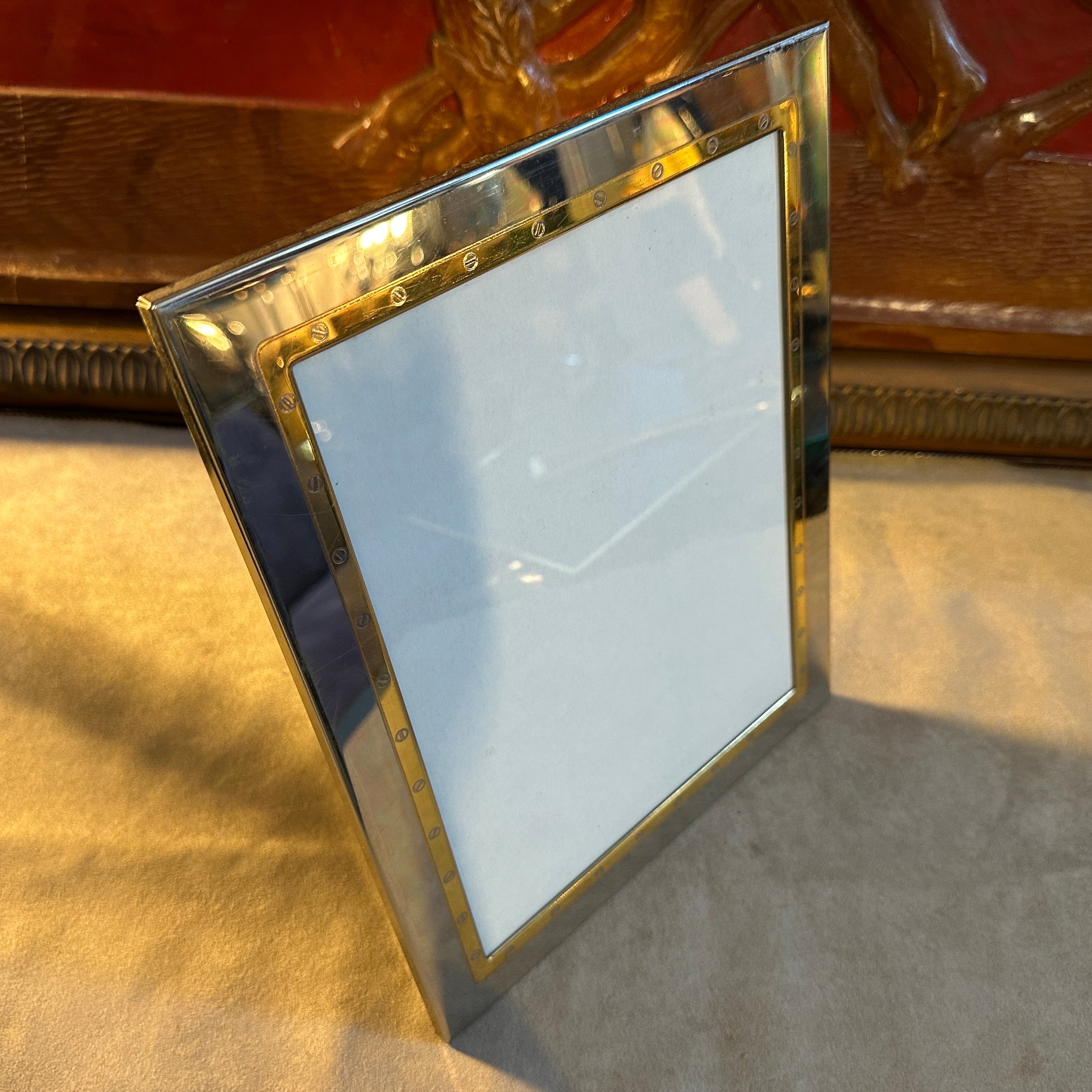Marco rectangular diseñado y fabricado en Italia en los años ochenta por MB Italy, el metal plateado y dorado recuerda el estilo de la casa Gucci de la época. Está en buen estado en general. Fabricado en chapa de plata de alta calidad con detalles