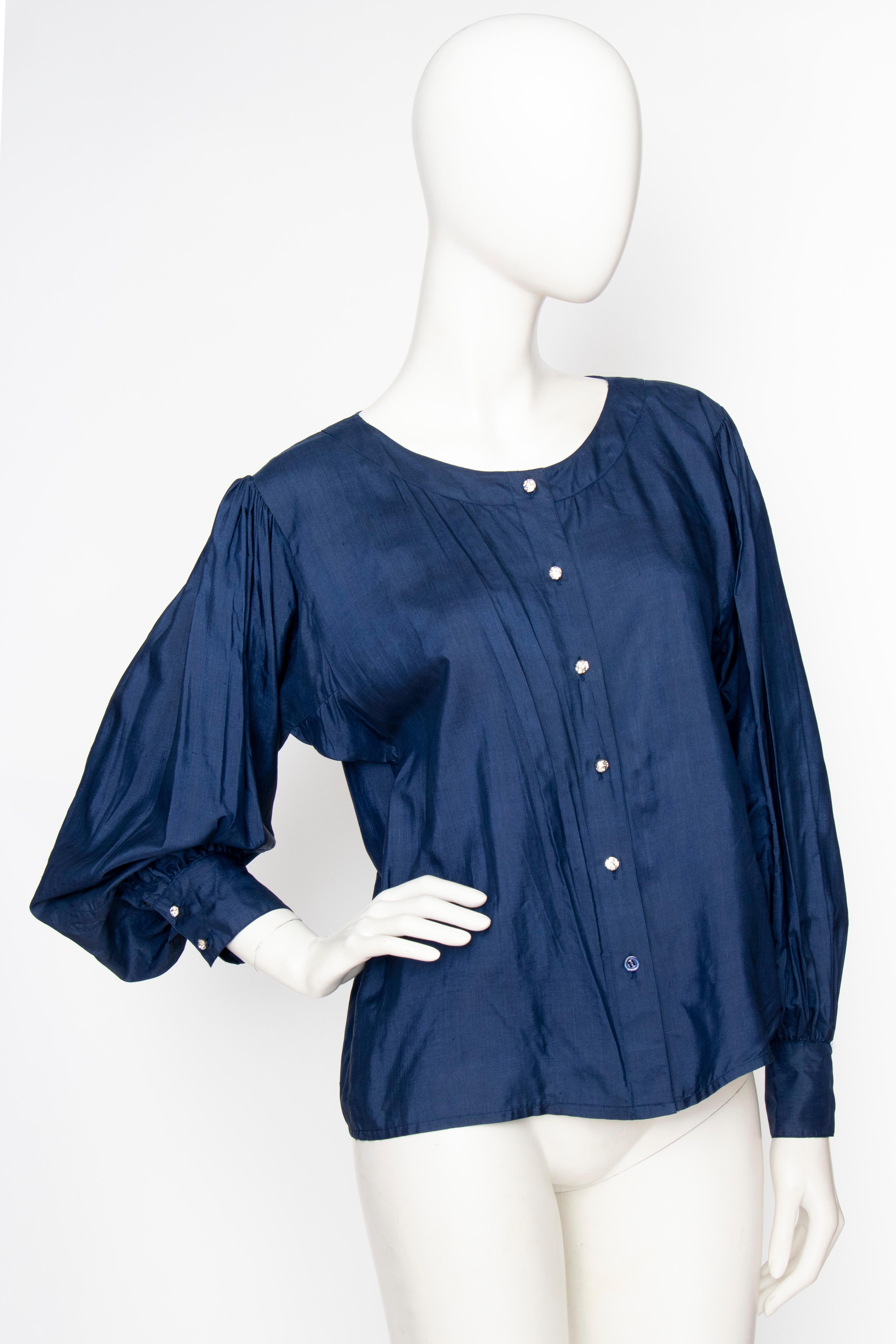 An early 1980s Yves Saint Laurent Rive Gauche blue silk blouse with a round neckline, a button-down front and voluminous sleeves. The blouse is unlined and has large clear rhinestone-studded buttons. 

The size corresponds to a modern size medium,