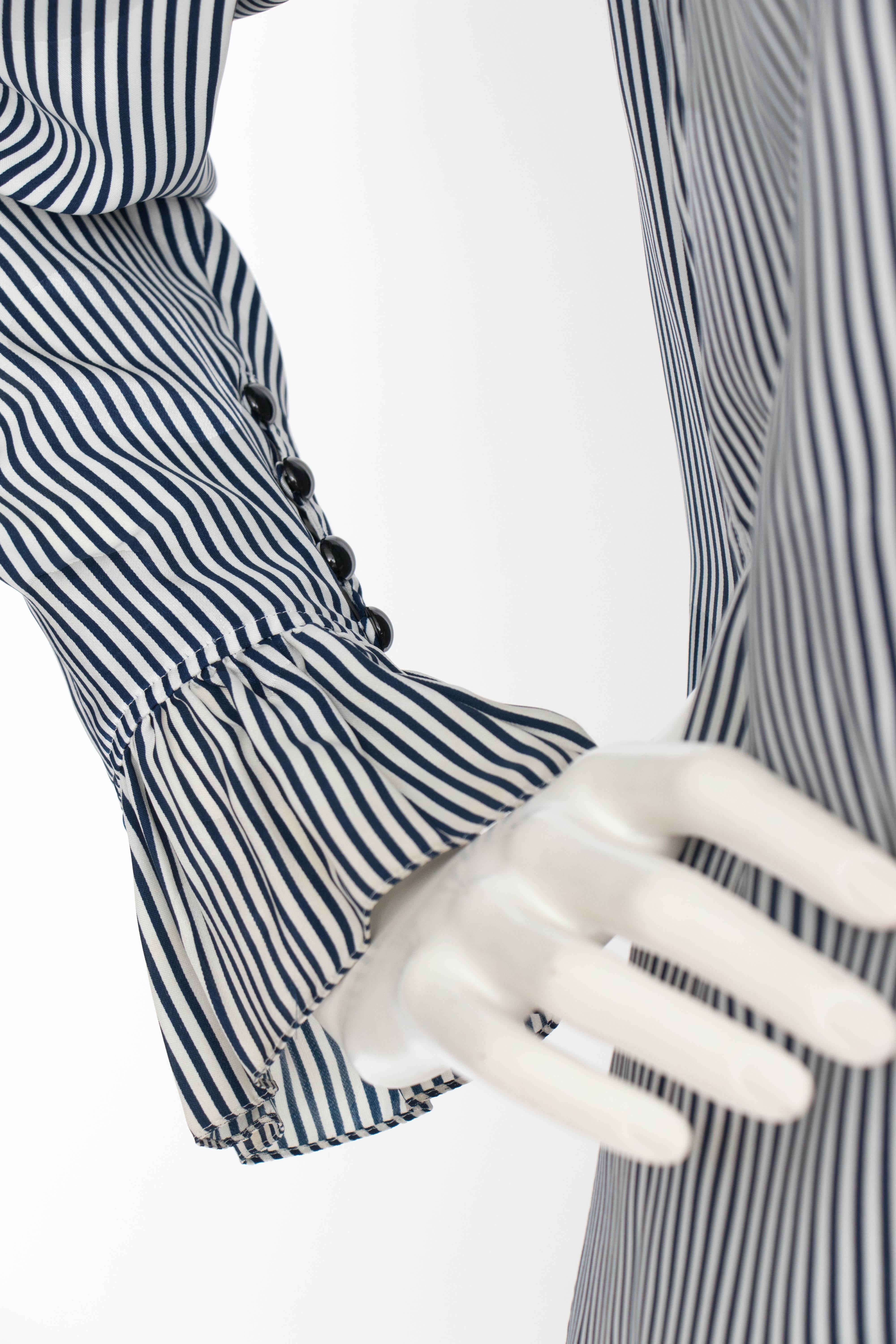 A 1980s Yves Saint Lauren blue and white stripe silk blouse with a ruffle collar and ruffle piping along each cuff. A subtle jacquard weave makes illusionist circles across the blouse. 

The size of the blouse corresponds to a modern size small, but