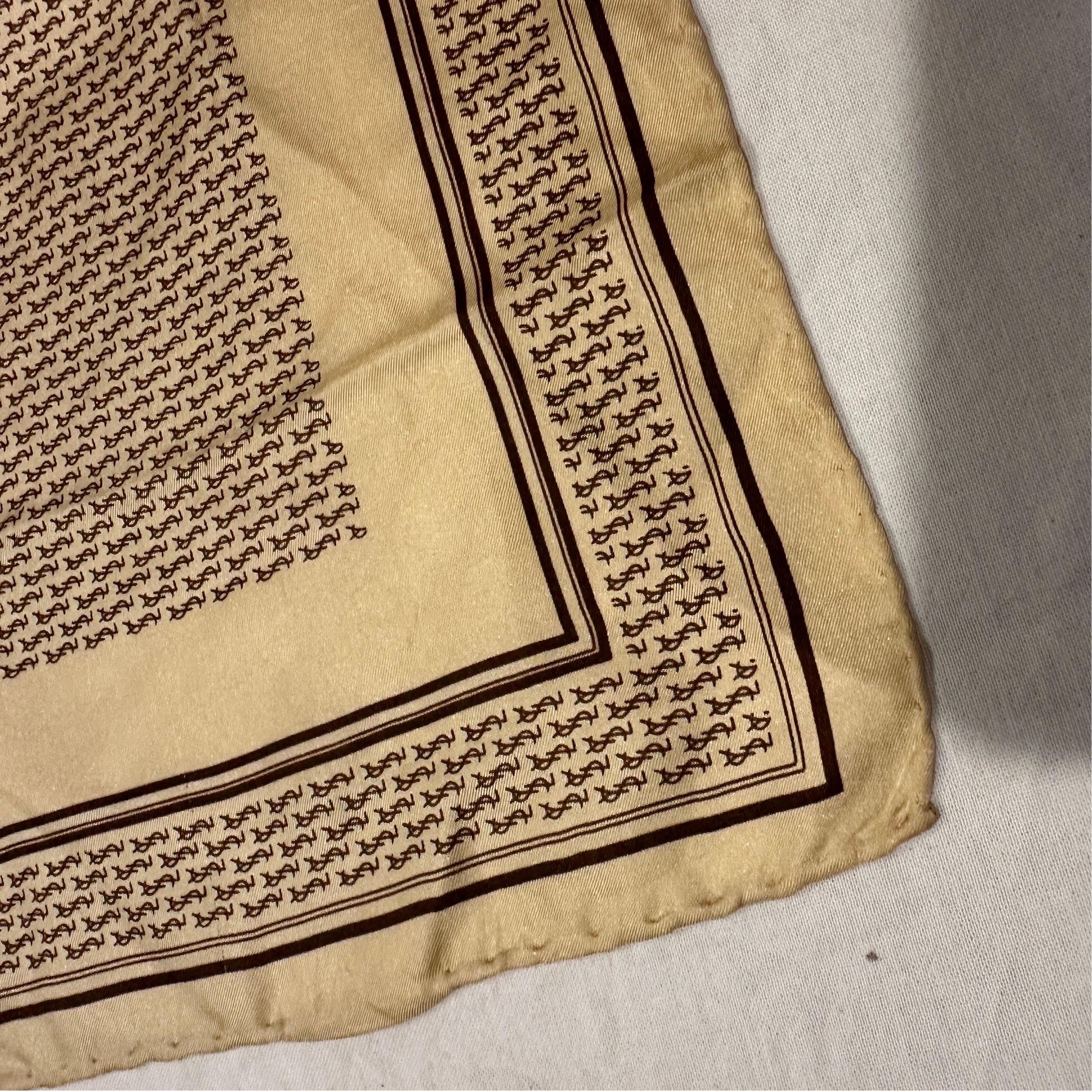 Questo autentico foulard di seta vintage di Yves Saint Laurent (YSL) degli anni '80 è un vero pezzo di storia della moda. Questo elegante accessorio quadrato presenta l'iconico Monogram YSL in un ricco motivo ripetuto su un luminoso sfondo beige o