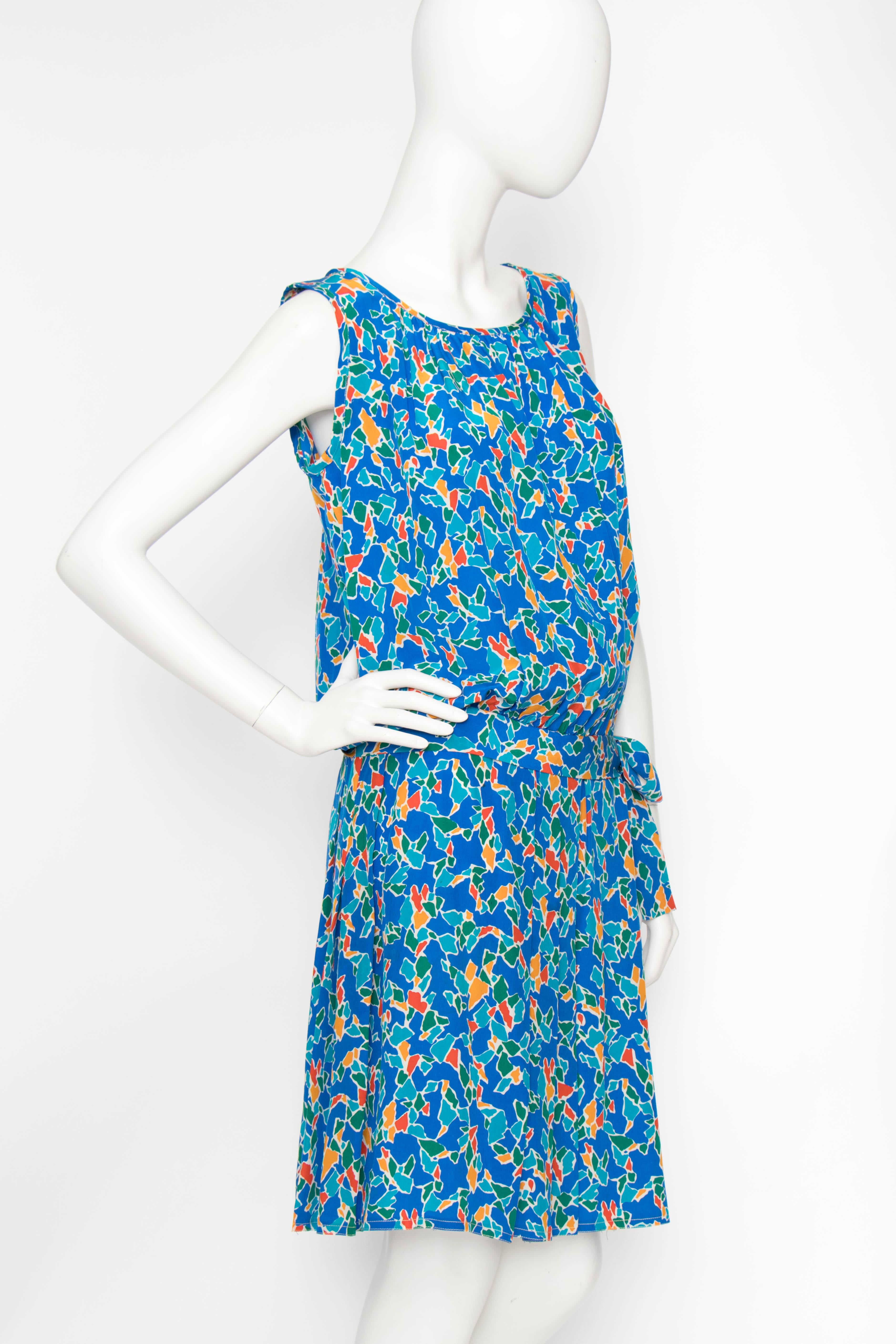 A 1980s Yves Saint Laurent Rive Gauche silk dress with a round neckline, pleated skirt and drop waist with bow detail. The sleeveless dress is clad in a fun graphic print in bold green, red, yellow and blue with white accents. 

The size of the