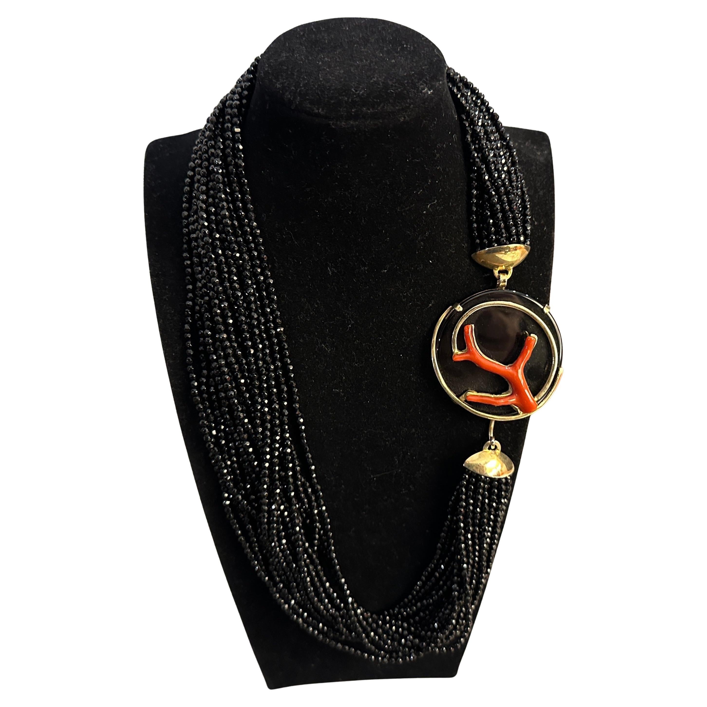 Diese exquisite italienische Halskette aus den 1990er Jahren ist eine harmonische Mischung aus Eleganz und kühnem Design, mit schwarzen Onyxperlen und einem auffälligen Mittelstück aus mediterraner Koralle. Die mehrsträngige Konstruktion besteht aus