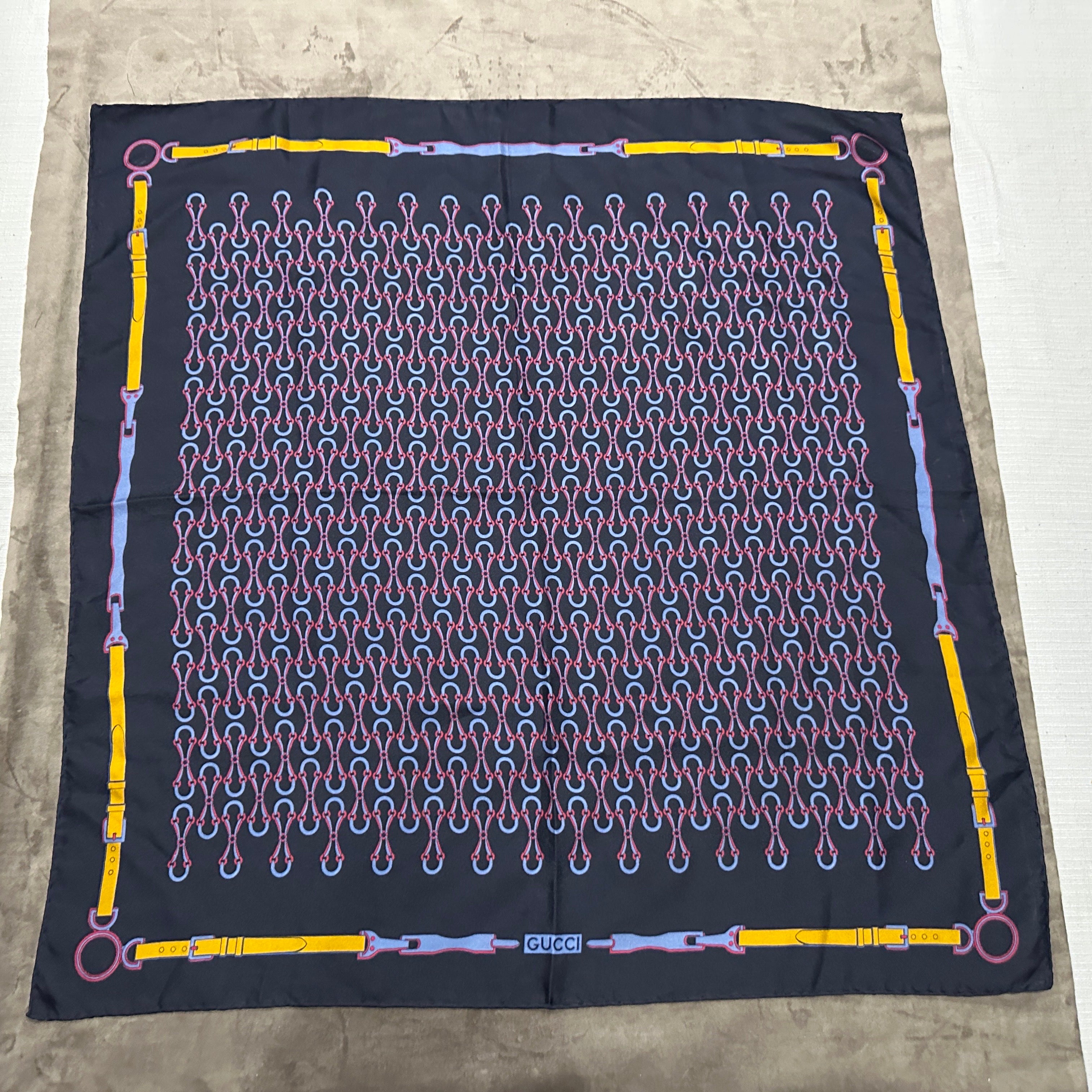 Questo elegante foulard vintage in seta di Gucci, prodotto in Italia negli anni '90, mette in mostra il classico patrimonio equestre del marchio con un design audace e intricato. Su uno sfondo blu scuro, la sciarpa presenta un motivo ripetuto di
