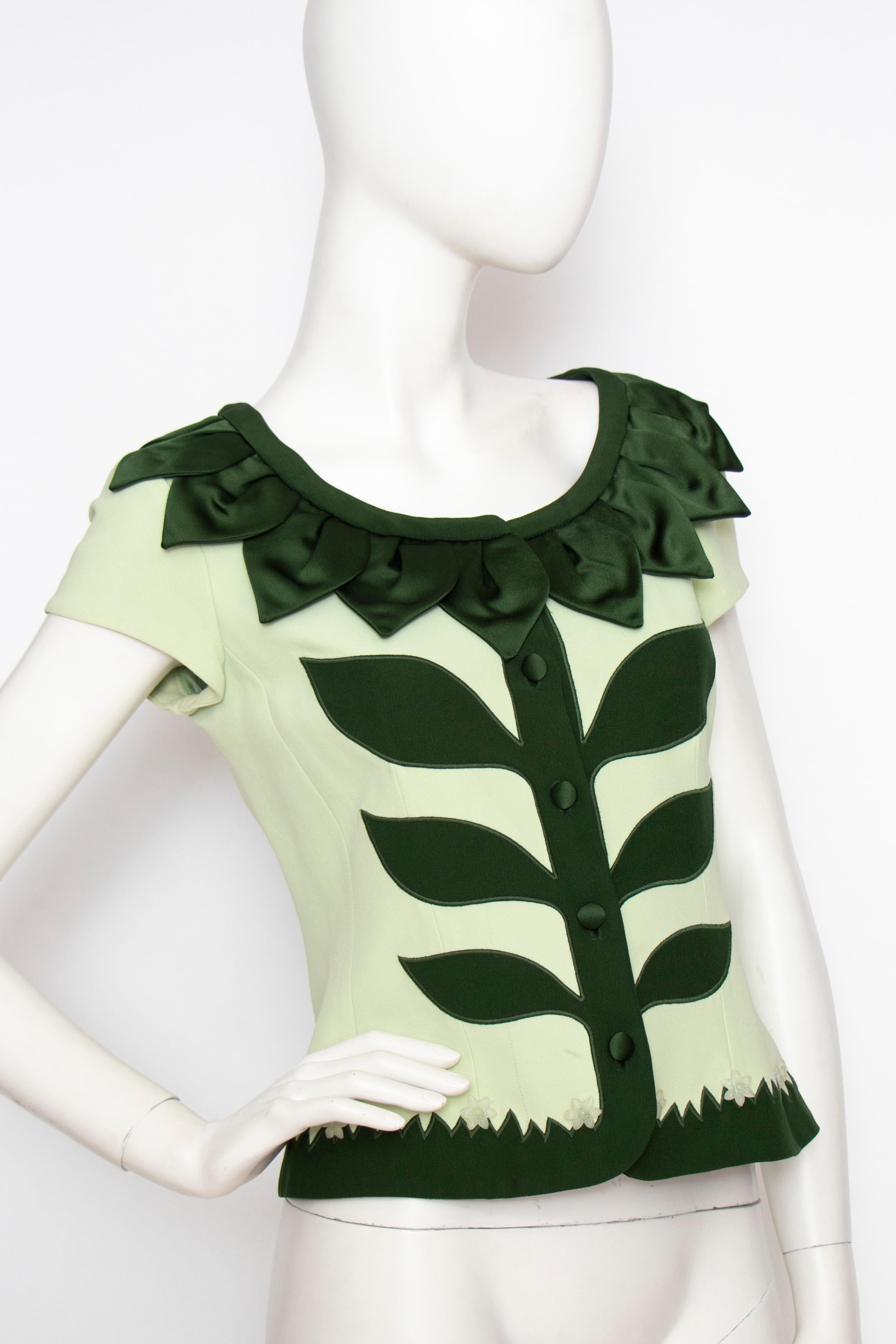 A fun 90s vintage Moschino Cheap and Chic elaborate min green crêpe blouse/jacket with appliquées in forest green, shaping a flower and green field accented with translucent flower buttons.

The size of the garment corresponds to a modern size