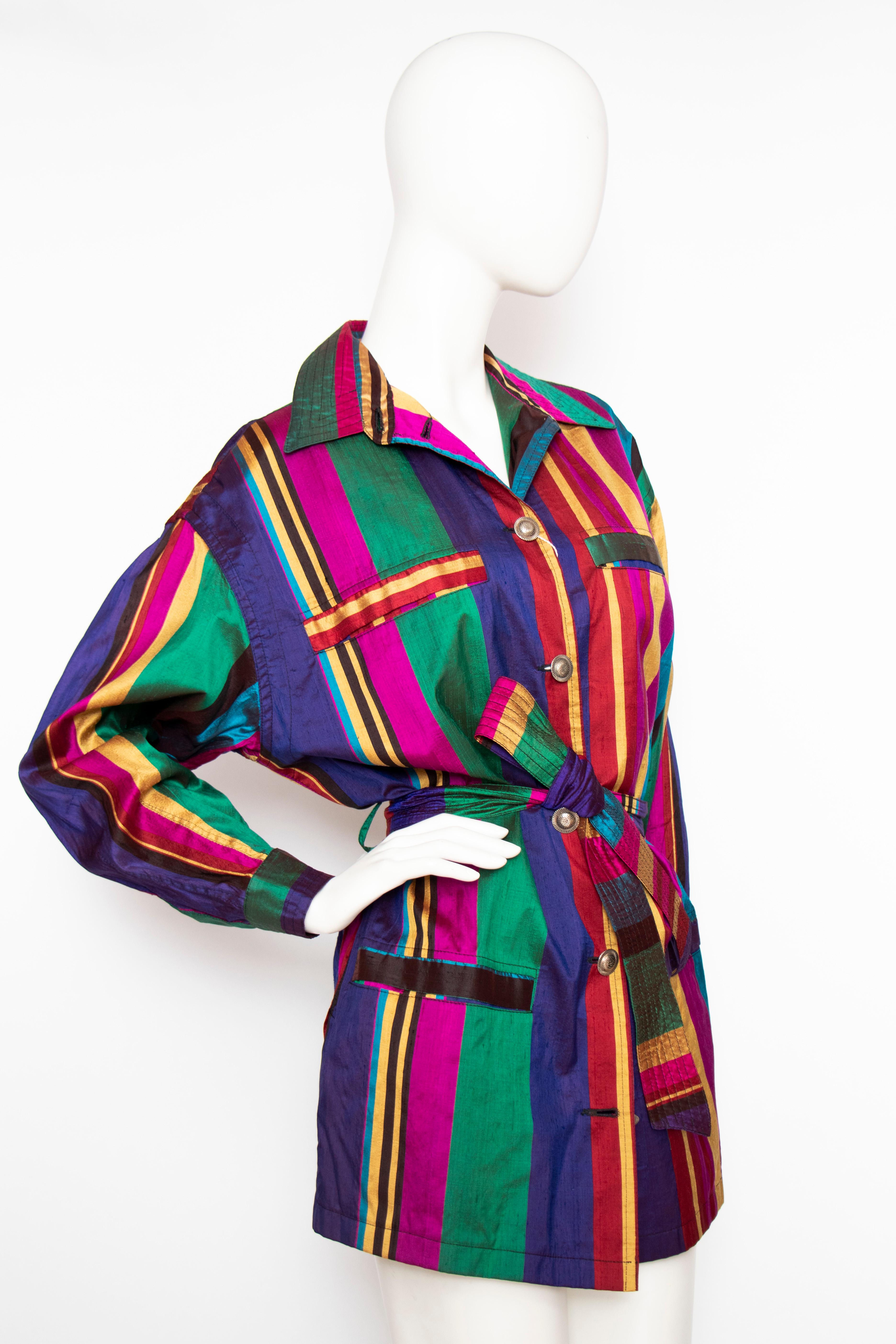 A 1990s vintage Versace Sport Thai silk trench jacket with a buttoned-down front, multiple pockets and a matching waist-belt. The beautiful silk is held in deep bright colours and the silver-toned buttons are engraved. 

The jacket is unlined.

The
