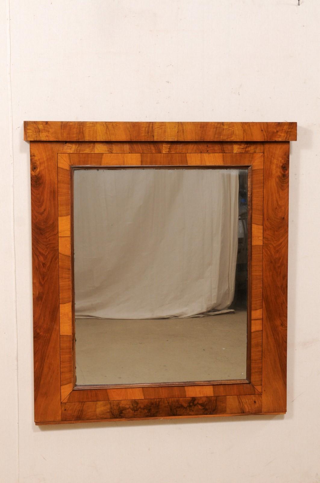 An Austrian Biedermeier style mirror from the 19th century. This antique mirror from Austria features it's original glass mirror and walnut veneer surround. The design is simple and clean, with a straight crest rail along the top. This piece is in