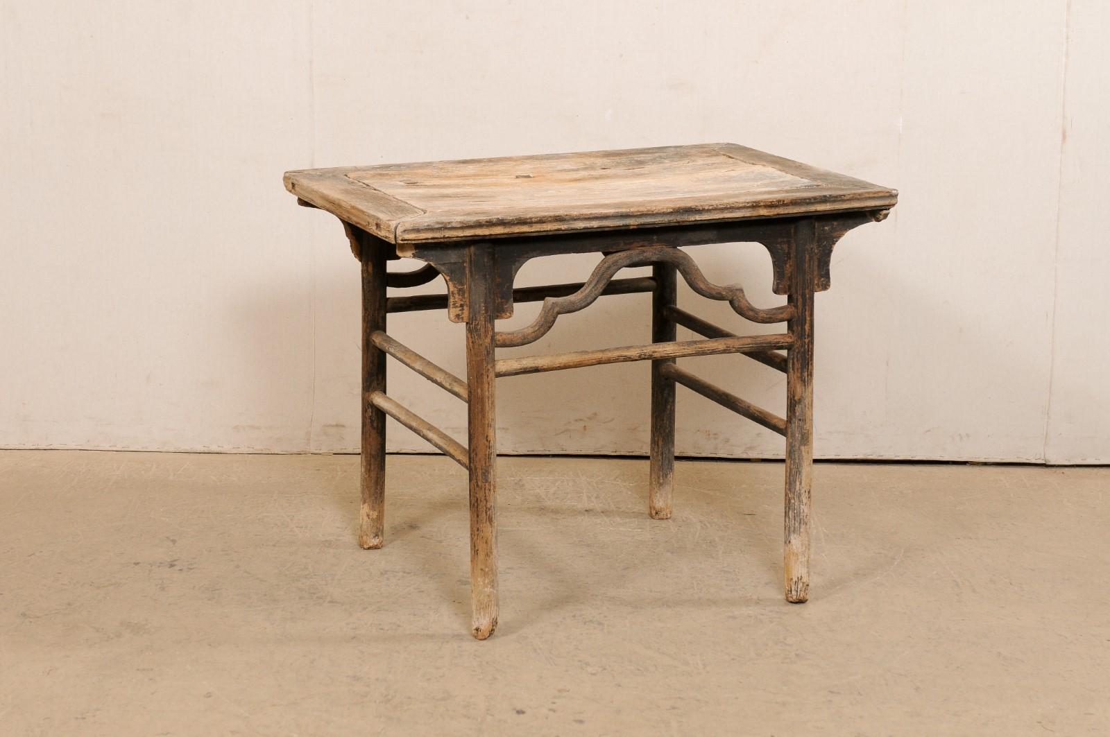 A Chinese wooden occasional table from the 19th century. This beautifully-rustic antique table from China features a framed-board and rectangular-shaped top with fabulous old joinery repairs, with carved-brackets supporting it's underside and curvy