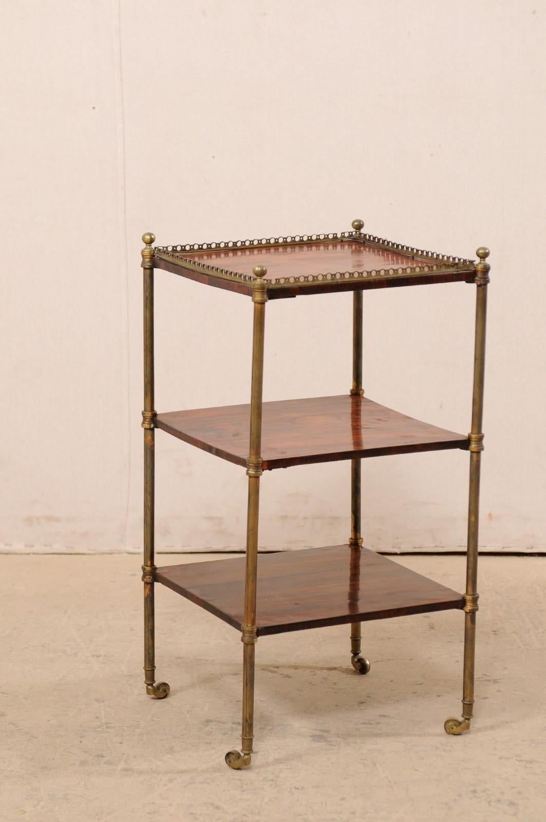 An English tiered rosewood table with brass accents from the late 19th century. This antique table from England has been made of beautiful rosewood for it's top and two lower shelves, set within four slender and rounded brass legs with finial