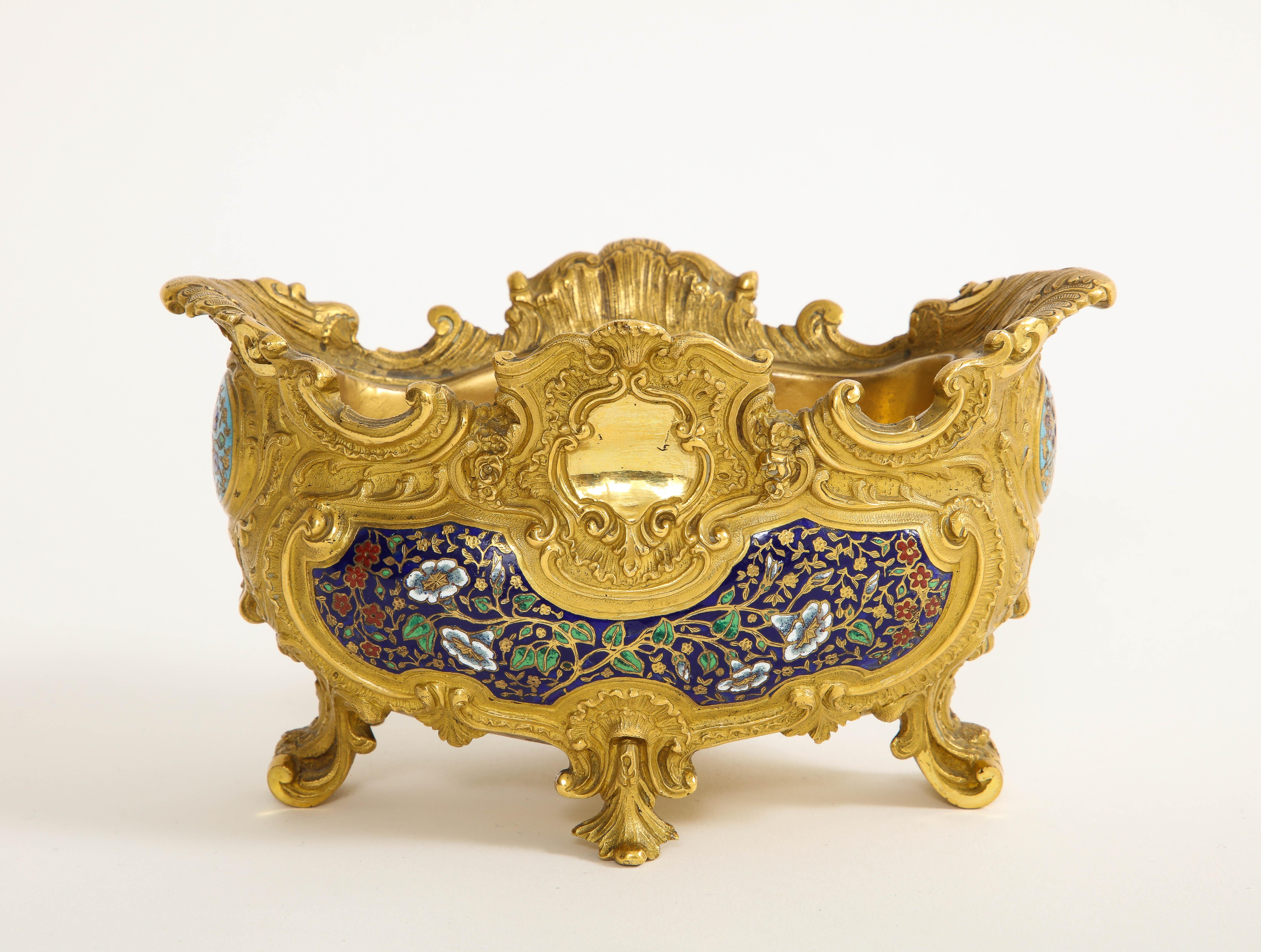 An Incredible 19th Century French Ormolu Champlevé Enamel Footed Centerpiece, Att. Barbedienne.  This captivating piece stands as a testament to the impeccable craftsmanship of its era. Elevated on resplendent acanthus scrolled feet, this enameled