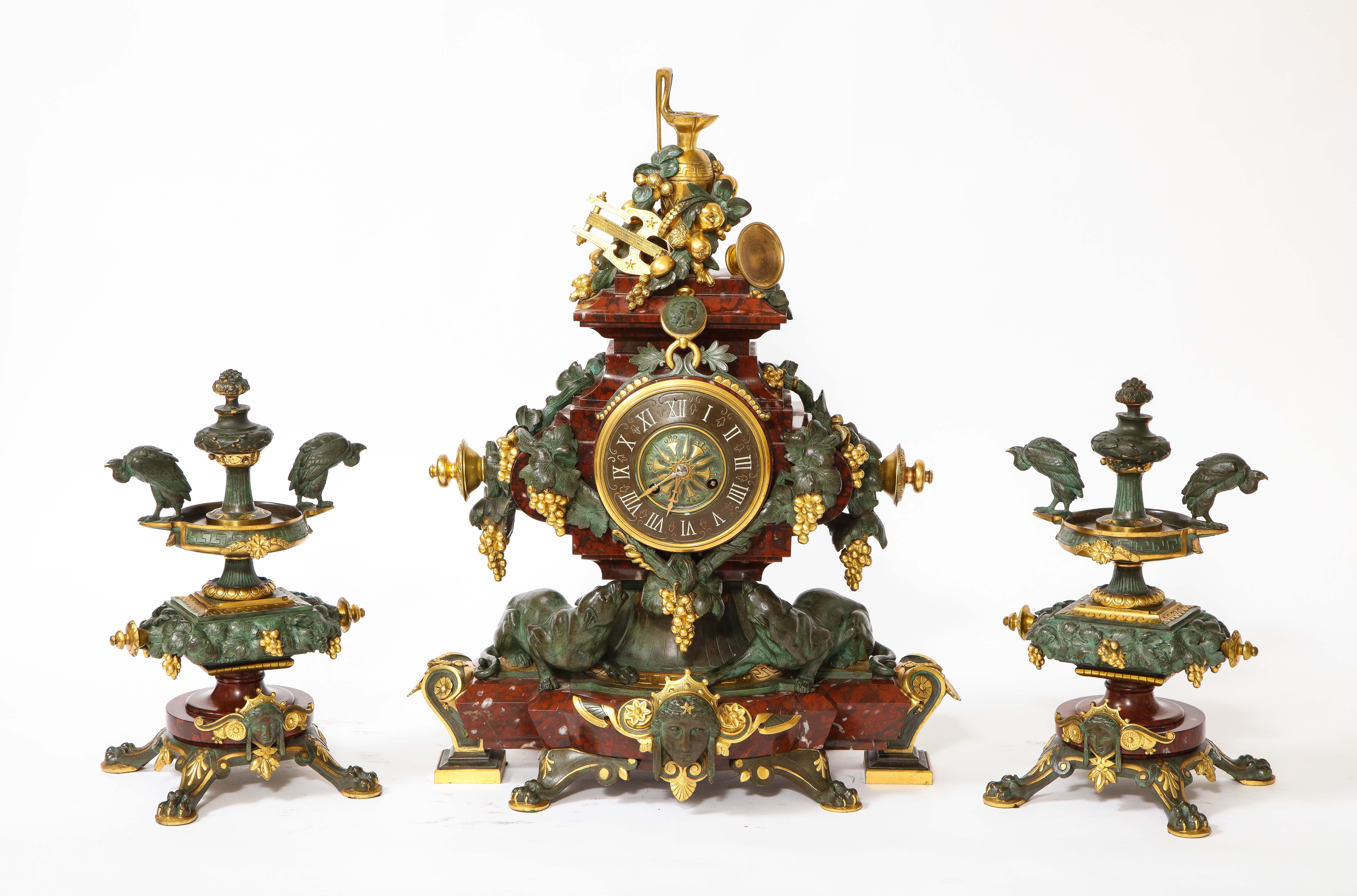 A Very Unusual and Quite Rare 19th Century French brown and green Patinated Bronze & Ormolu Mounted Rouge Marble Clock Garniture.  This three-piece garniture set, comprising a central mantel clock and a pair of matching tazze, is executed in