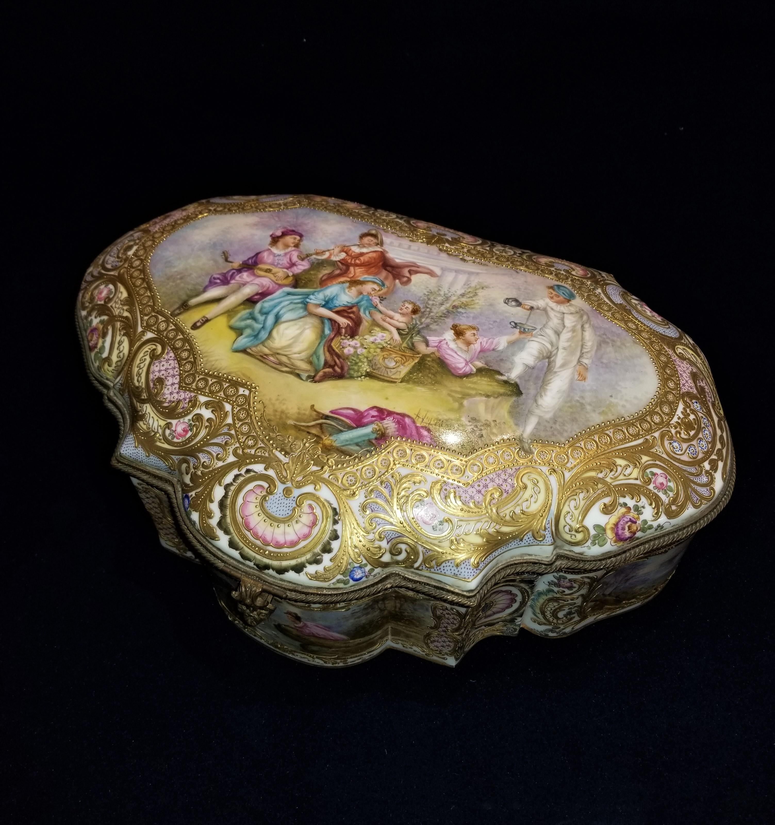 A beautiful 19th century gilt bronze mounted sevres jewel box and cover with multi-panel scenes. Of cartouche shape, the top painted with two maidens reclining in a garden attended by Cupid, two musicians and the Commedia dell'Arte figure Pierrot