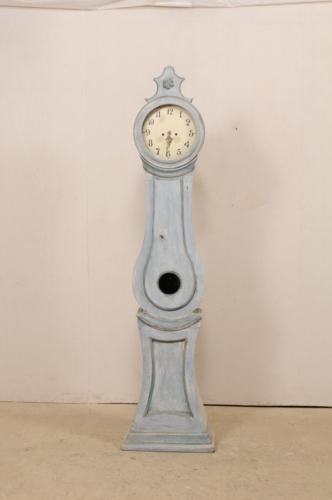 A Central Swedish 19th century long-case floor clock. This antique floor clock from central Sweden is crowned with an exaggerated carved crest atop it's head with delicate flower at center. Trimmed details accentuate it's neck and underside of the