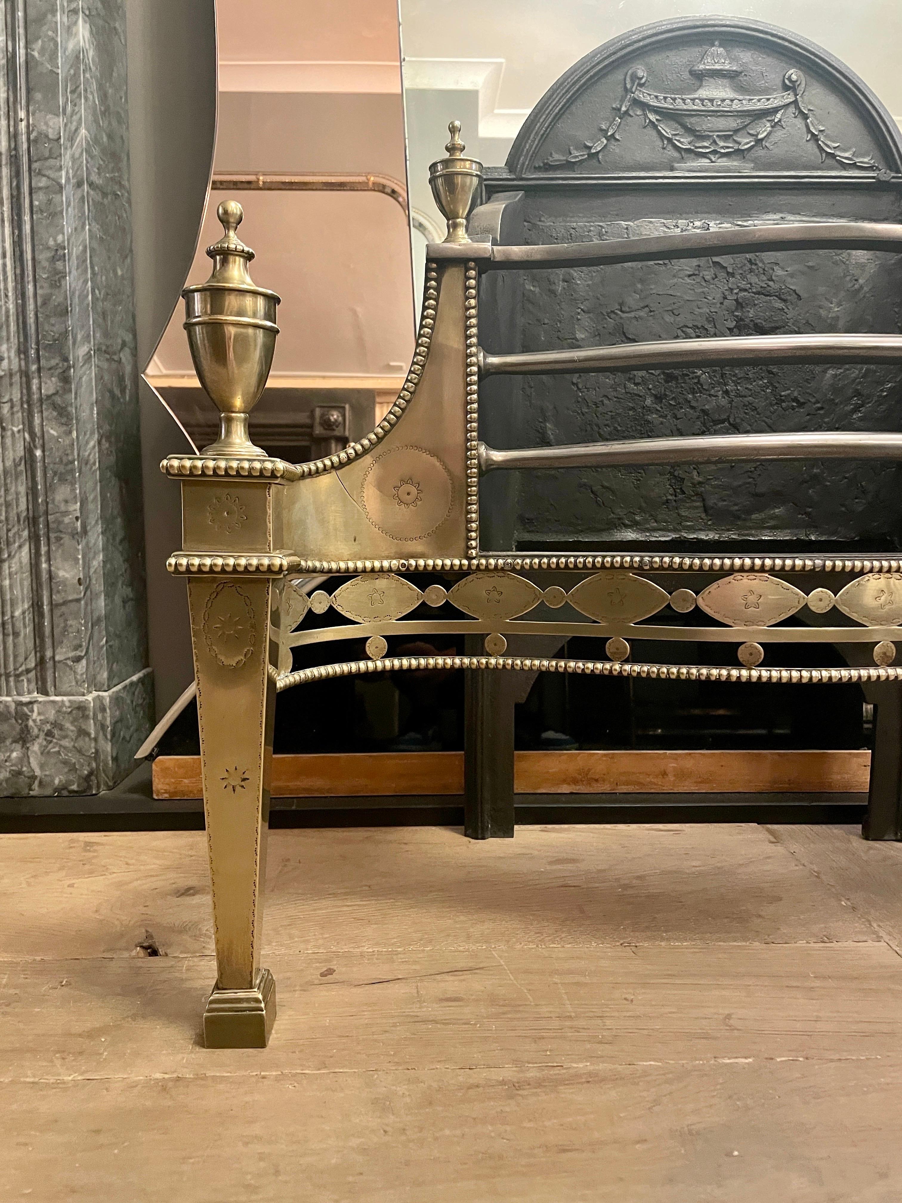 An English Adam style fire grate in polished brass and wrought iron by 19th century renowned blacksmith Thomas Elsley. The ornate cut and pierced fret work beneath bowed wrought iron bars, flanked by brass wings. The supports tapering with matching