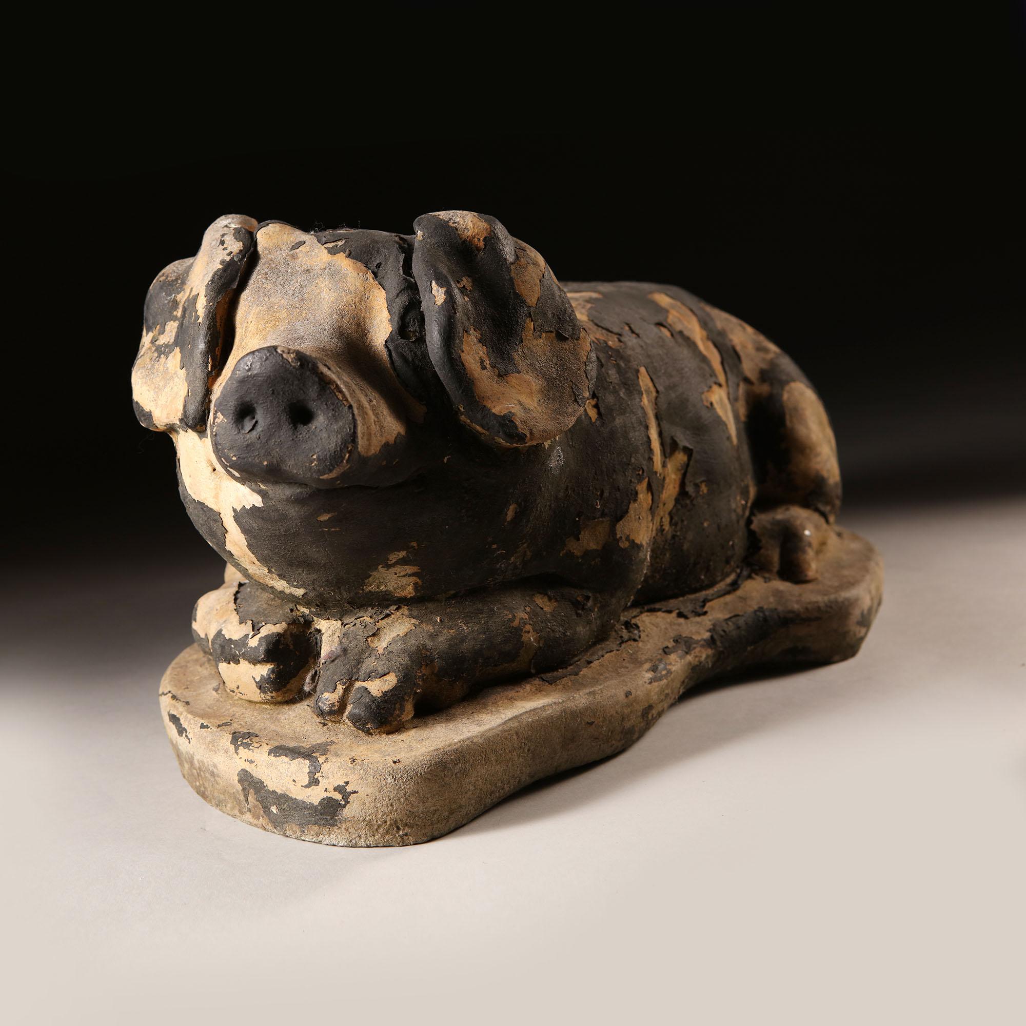 A late 19th century English animal sculpture, a stone model of a smiling pig lying down, with large ears, with remaining black paint residue.