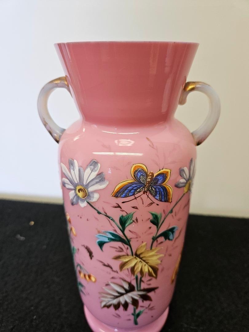 Antique French Pink Opaline cased glass hand decorated floral motif vase.  The flared neck at the top flanked buy two handles with hand decorated enamel all over. The floral and butterflies vibrantly colored. 9 inches tall, 6 inches wide handle to
