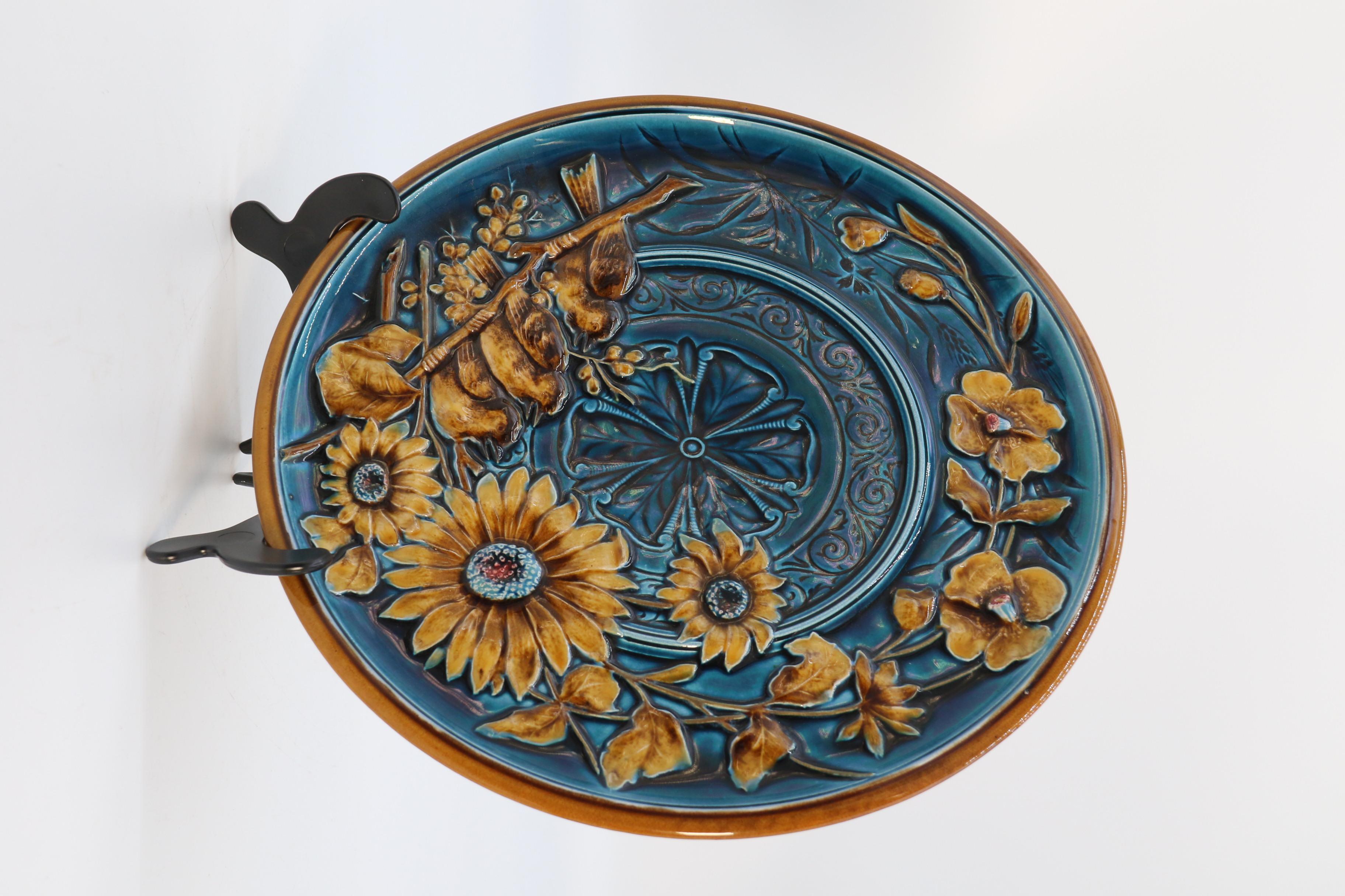 This rich three dimensionally decorated wall charger is a majolica pottery highly decorative example by the well regarded Austrian Gebruder Schutz factory. It is circular with a deep relief design of a naturalistic view of a row of three baby birds